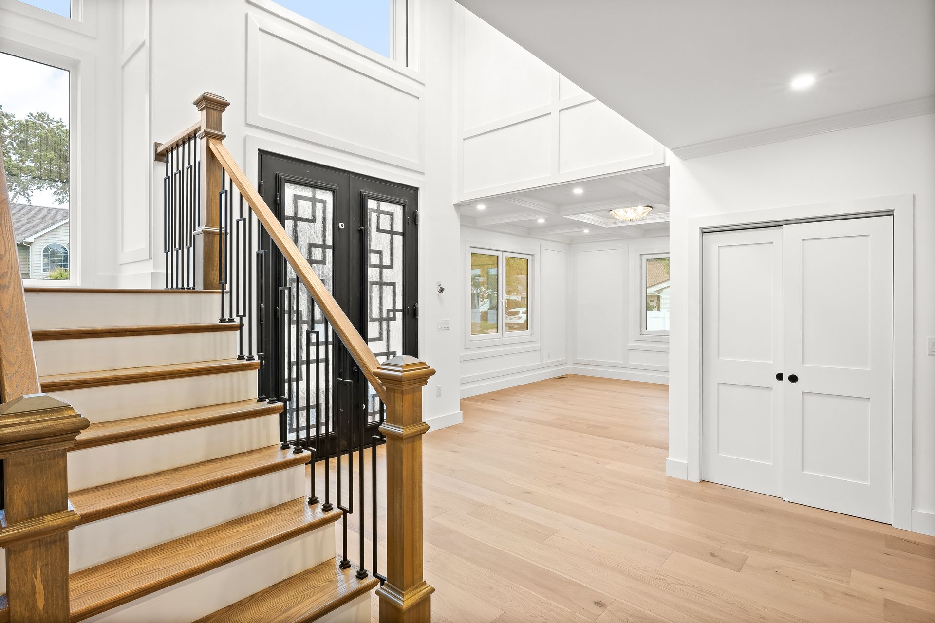 Bright foyer with hardwood floors, staircase, black front door, and white double closet doors