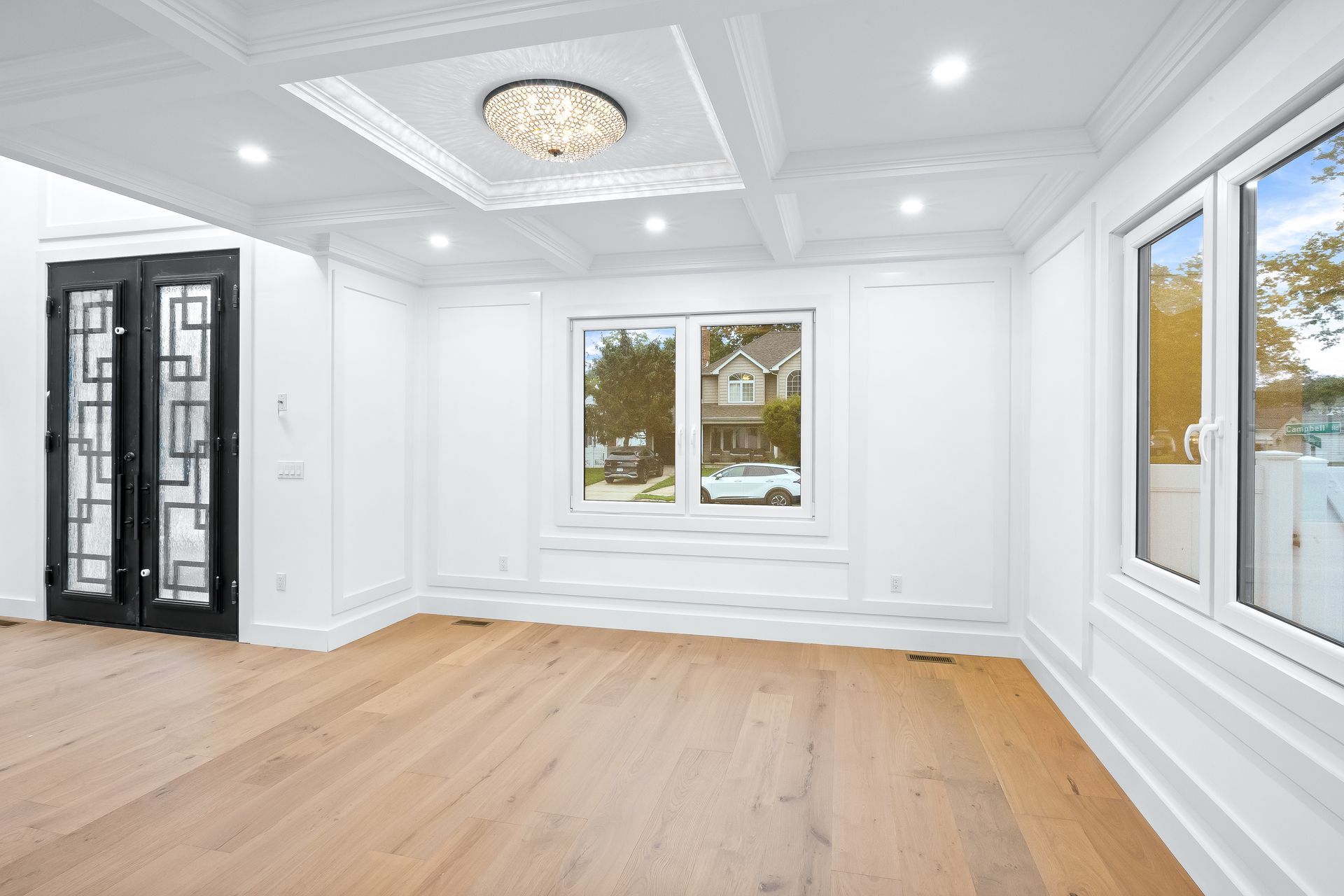 Bright empty living room with white walls, light wood floors, and large windows.