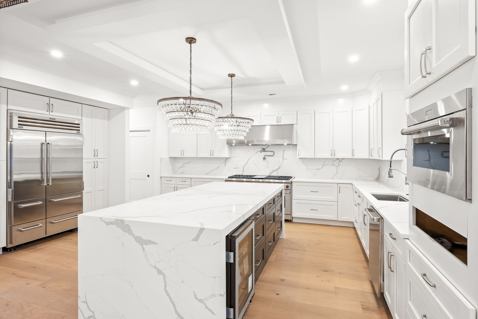 Bright white modern kitchen with marble island, stainless steel appliances, and wood floors