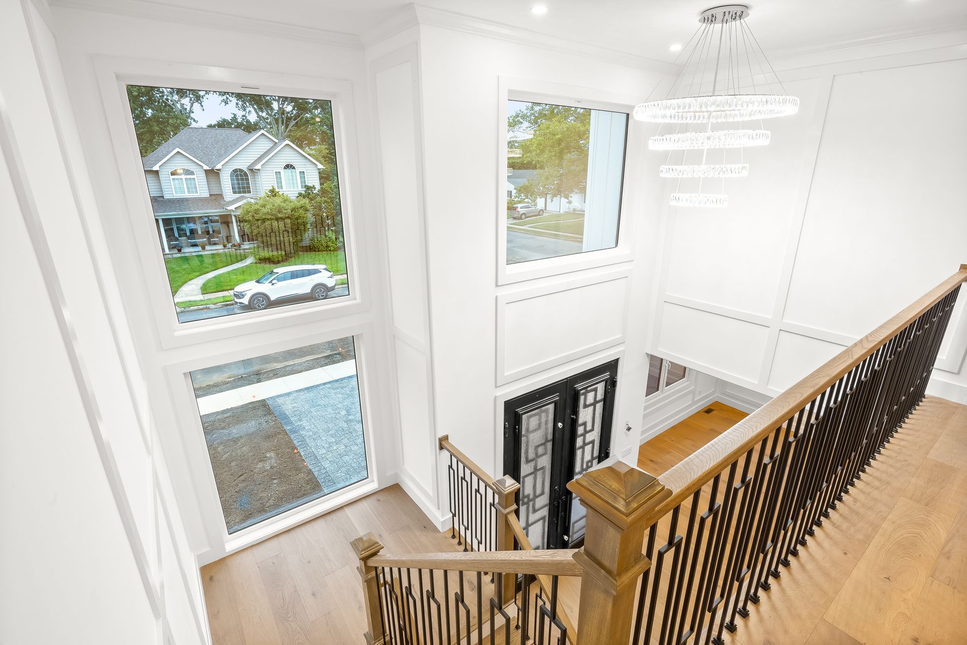 Bright foyer with staircase, white walls, wood floor, and large windows overlooking a neighborhood.