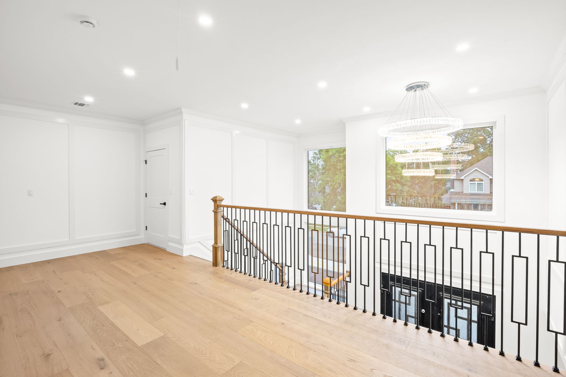 Bright white upstairs hallway with wood floors, railing, recessed lights, and large windows.