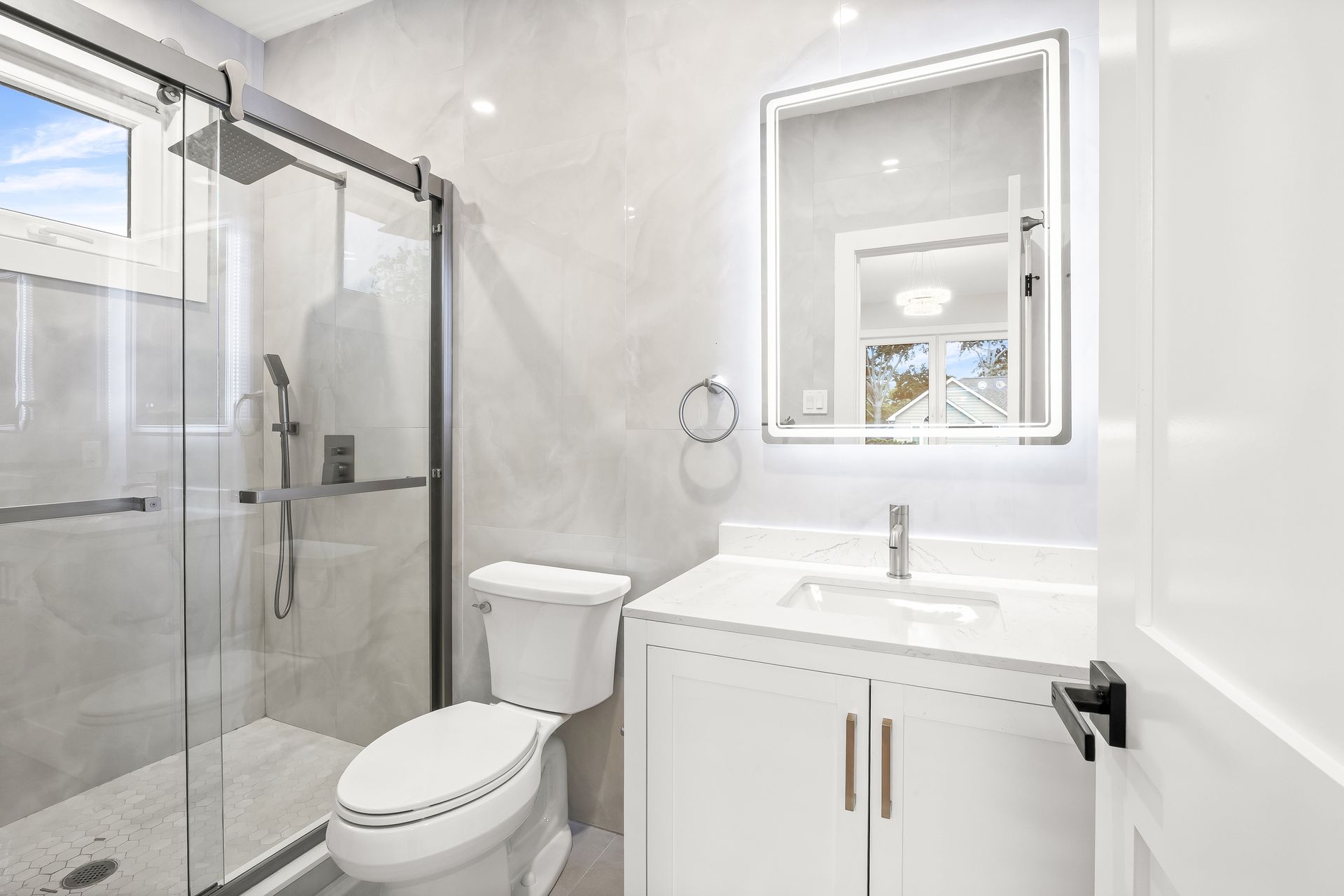 Bright modern bathroom with glass shower, toilet, white vanity, and lit mirror
