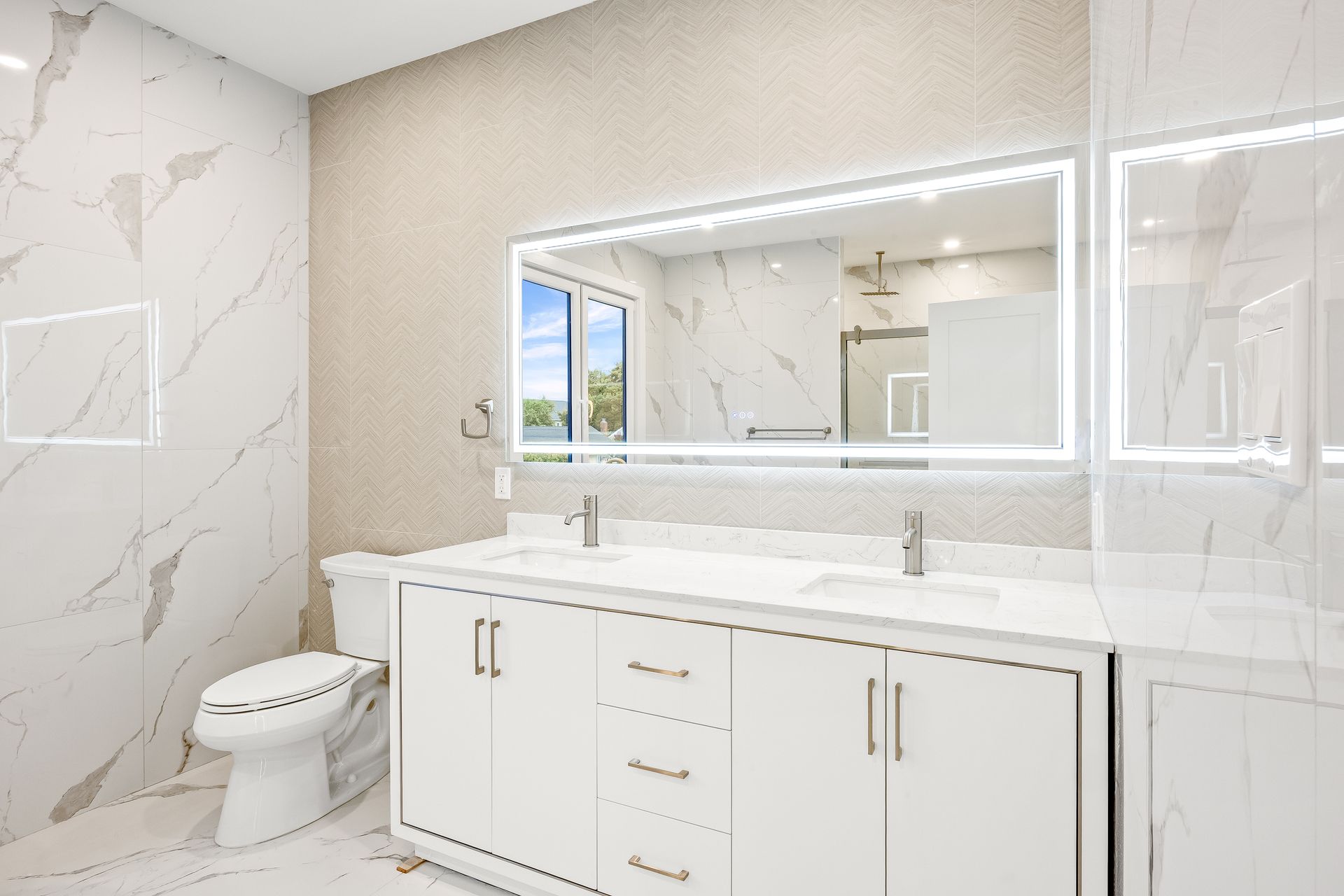 Bright white modern bathroom with double vanity, large mirror, and toilet beside marble-tile shower wall