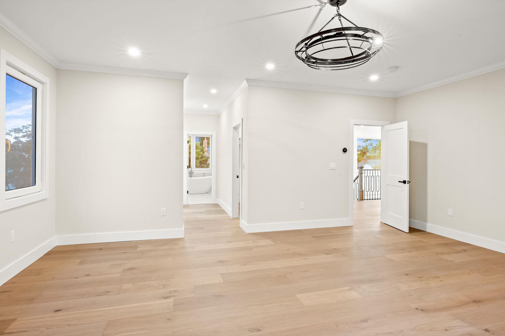 Empty modern living room with white walls, light wood floors, and a black ceiling light fixture