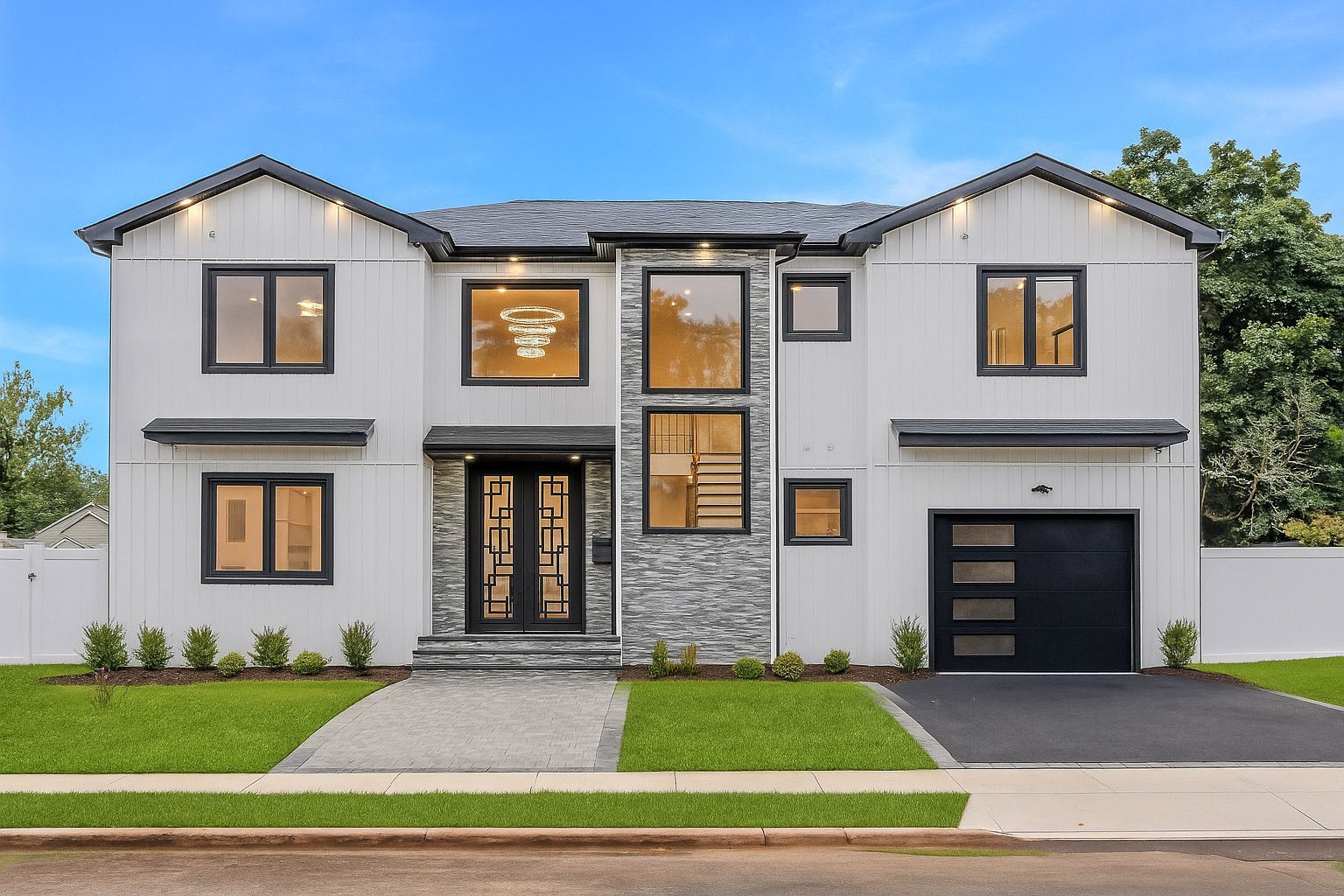 Modern two-story white house with black trim, front lawn, and double garage under a clear blue sky