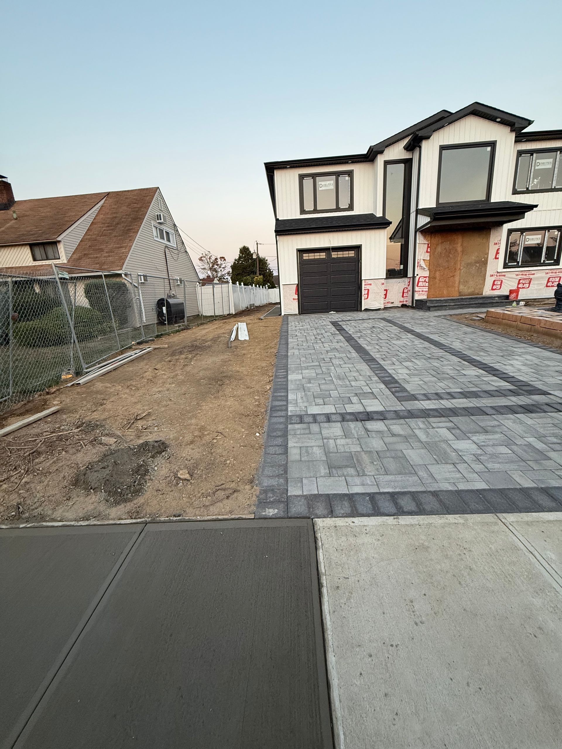 Suburban house with newly paved driveway beside a dirt front yard and neighboring homes.