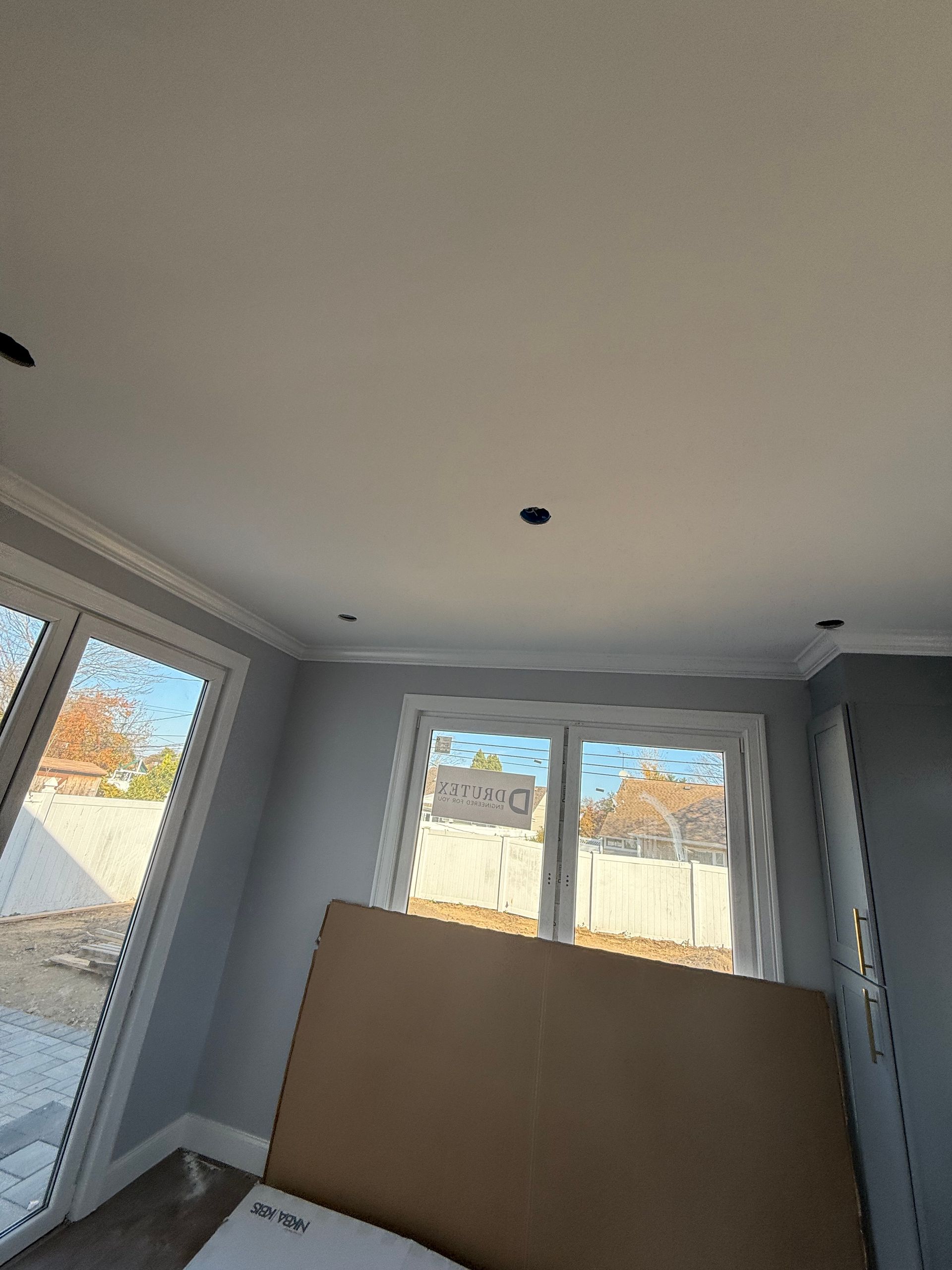 Empty gray room with windows and a leaning plywood board against the wall