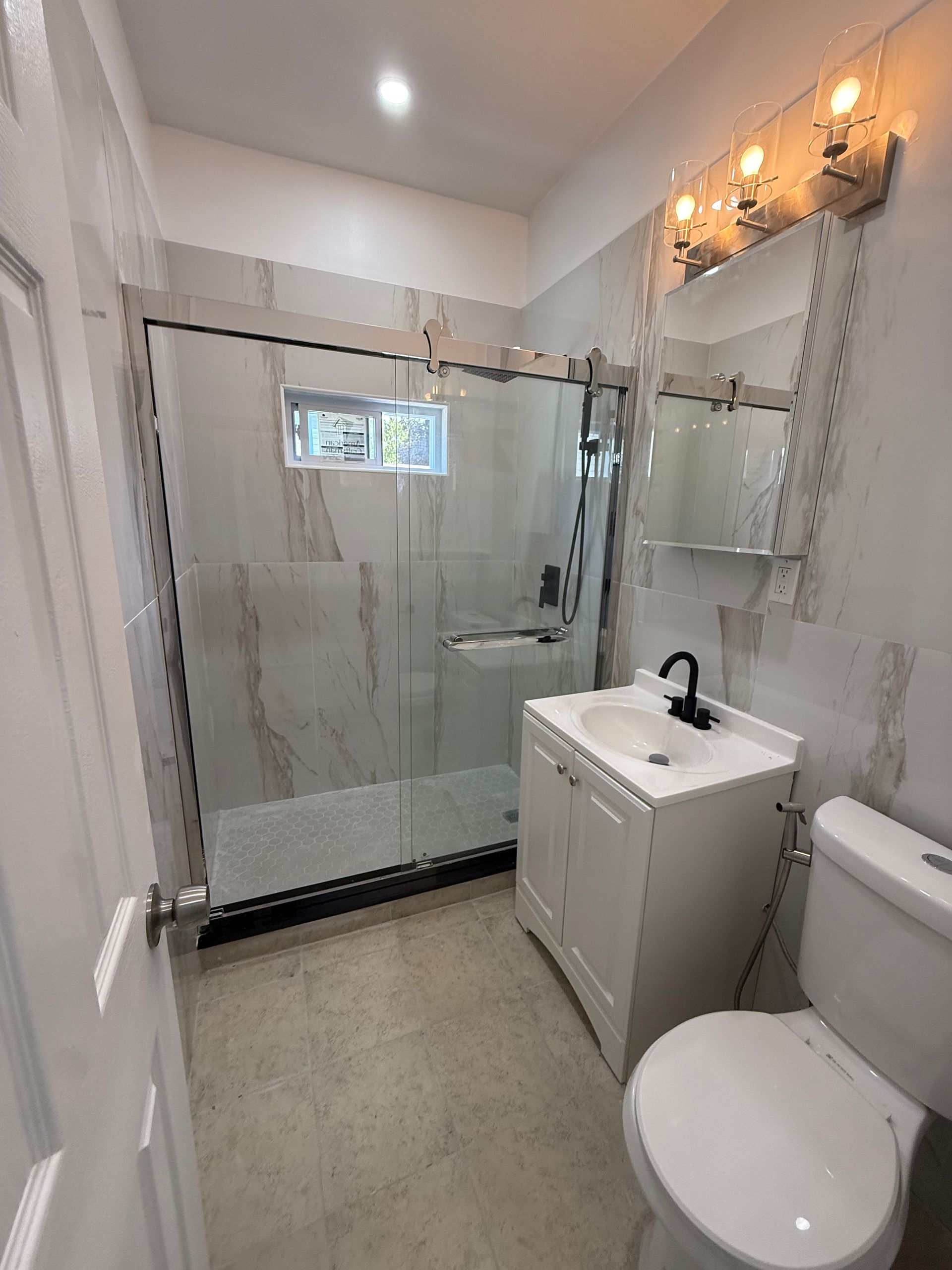 Small bathroom with glass shower, white vanity, toilet, and wall light fixtures.