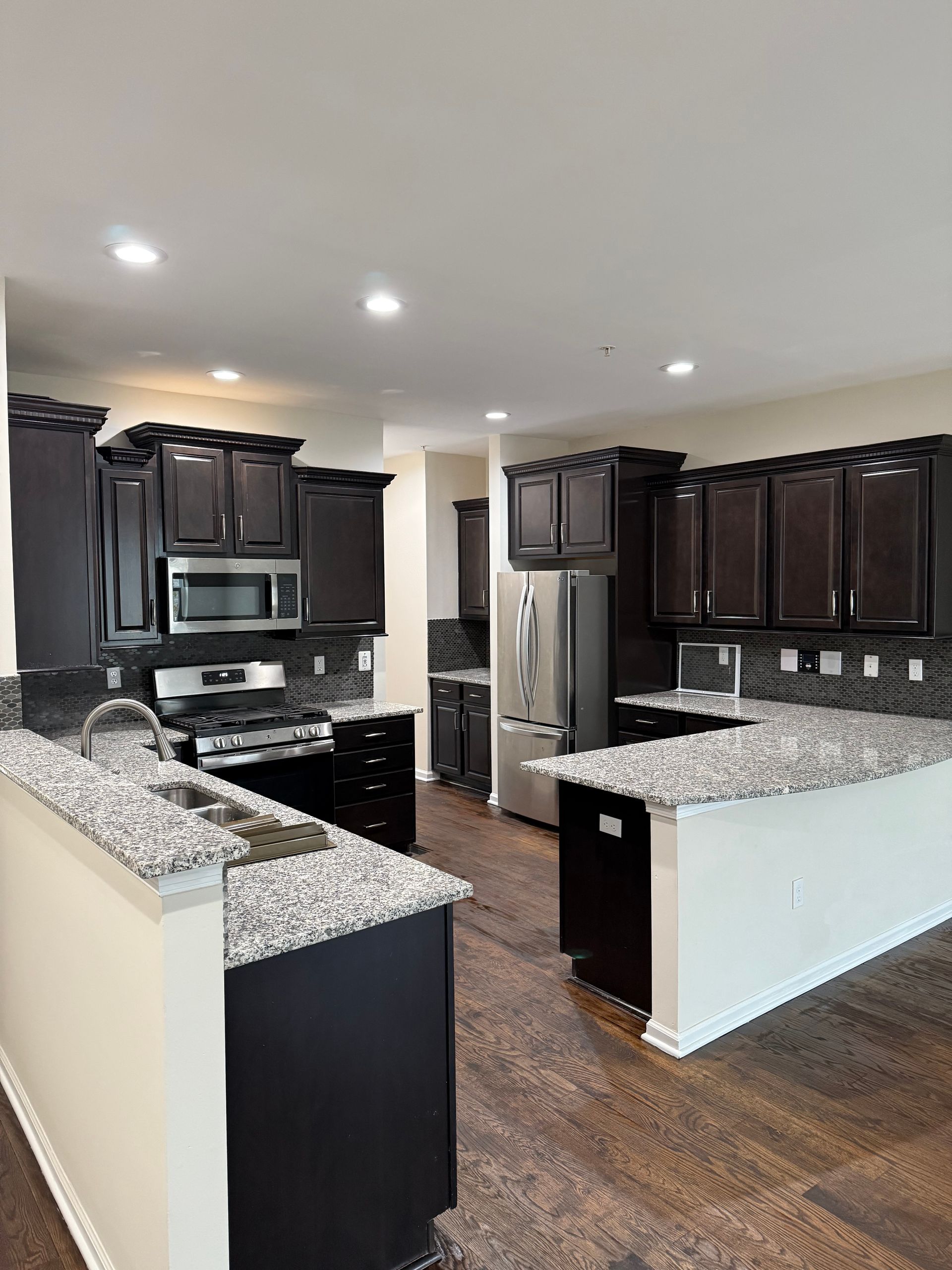 Modern kitchen with dark cabinets, granite countertops, stainless steel appliances, and wood floors