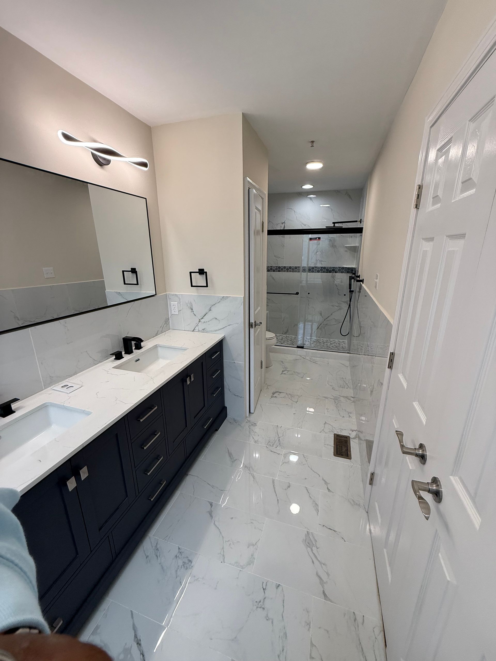 Modern bathroom with marble tile, dark vanity, large mirror, and glass shower enclosure.