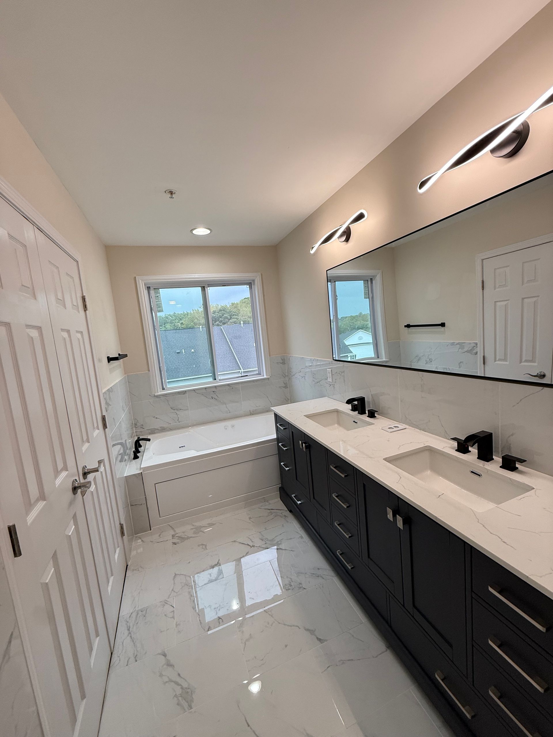 Bright bathroom with double vanity, large mirror, white tile floor, and window light