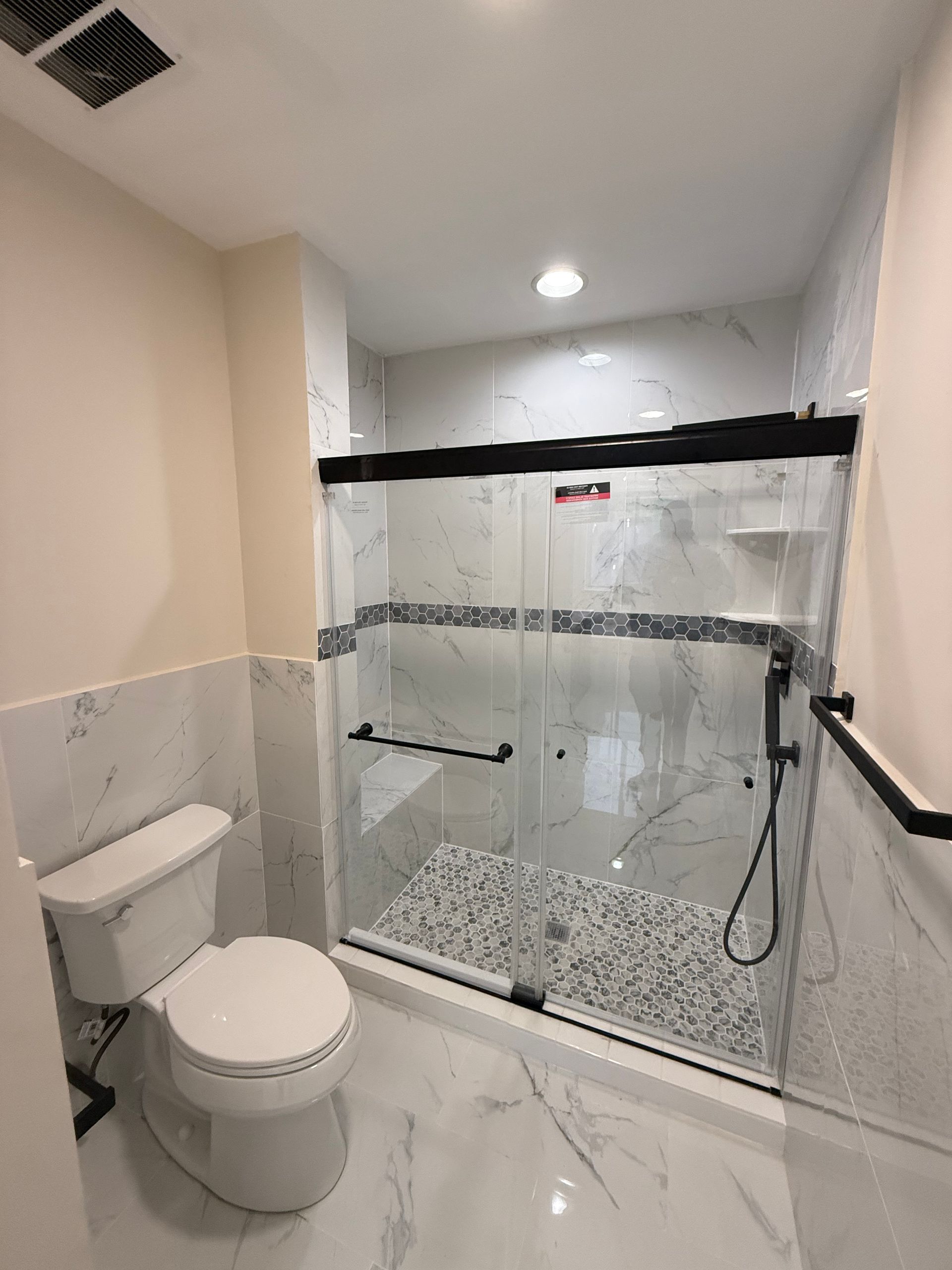 Small bathroom with toilet and glass shower enclosure, white tile walls and floor.