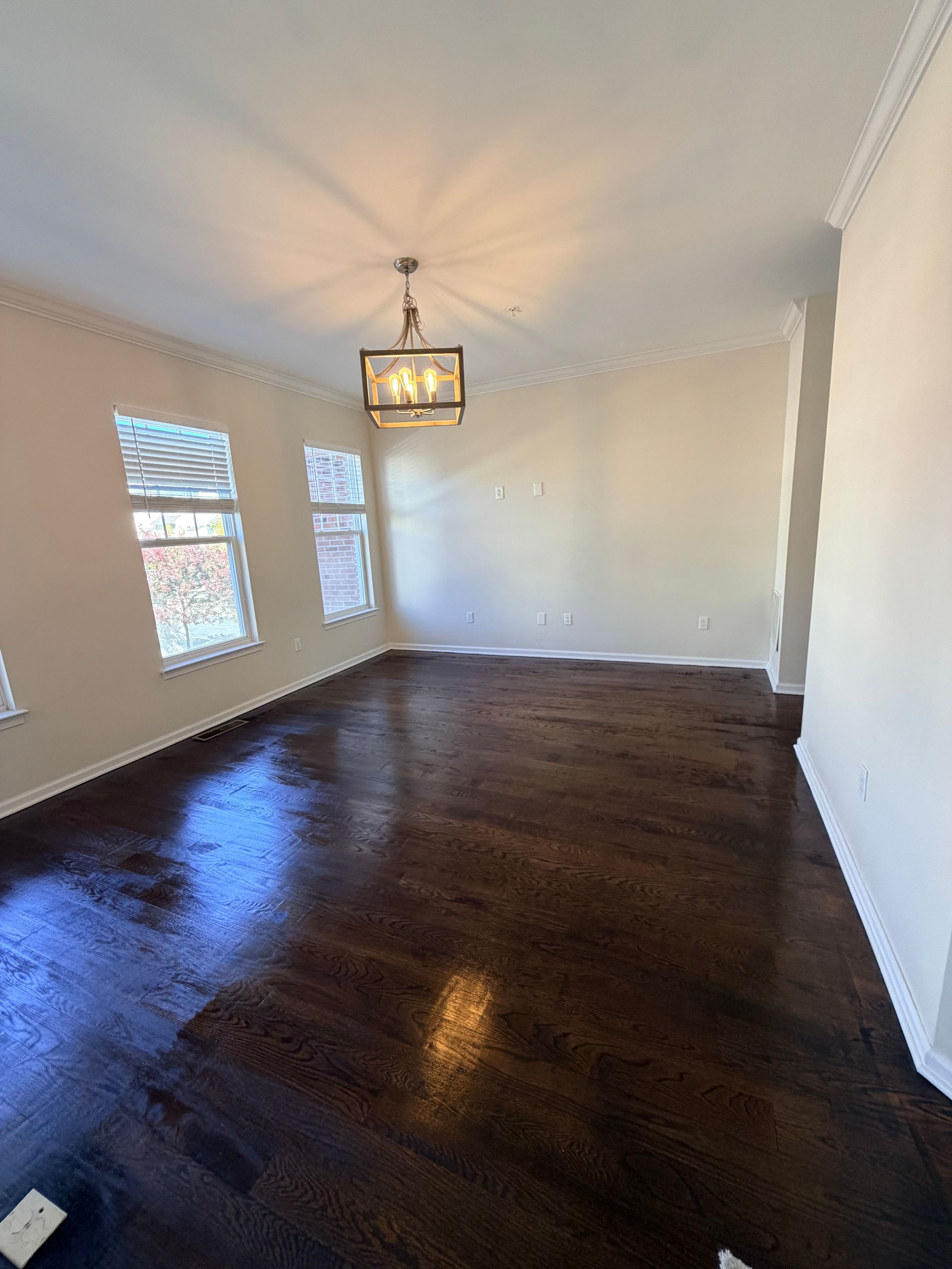 Empty dining room with dark hardwood floors, white walls, and a hanging light fixture.