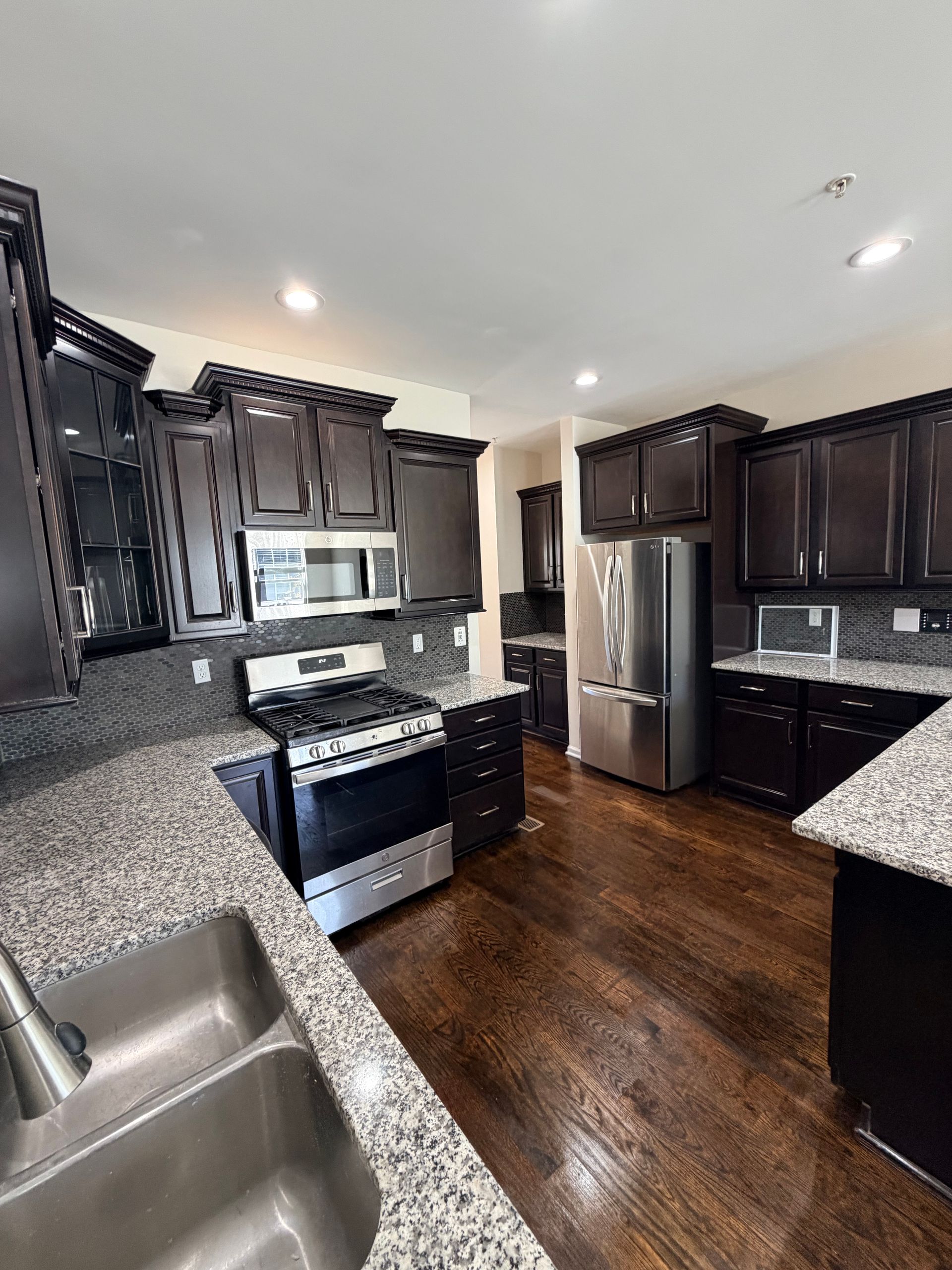 Modern kitchen with dark cabinets, granite counters, stainless appliances, and hardwood floors