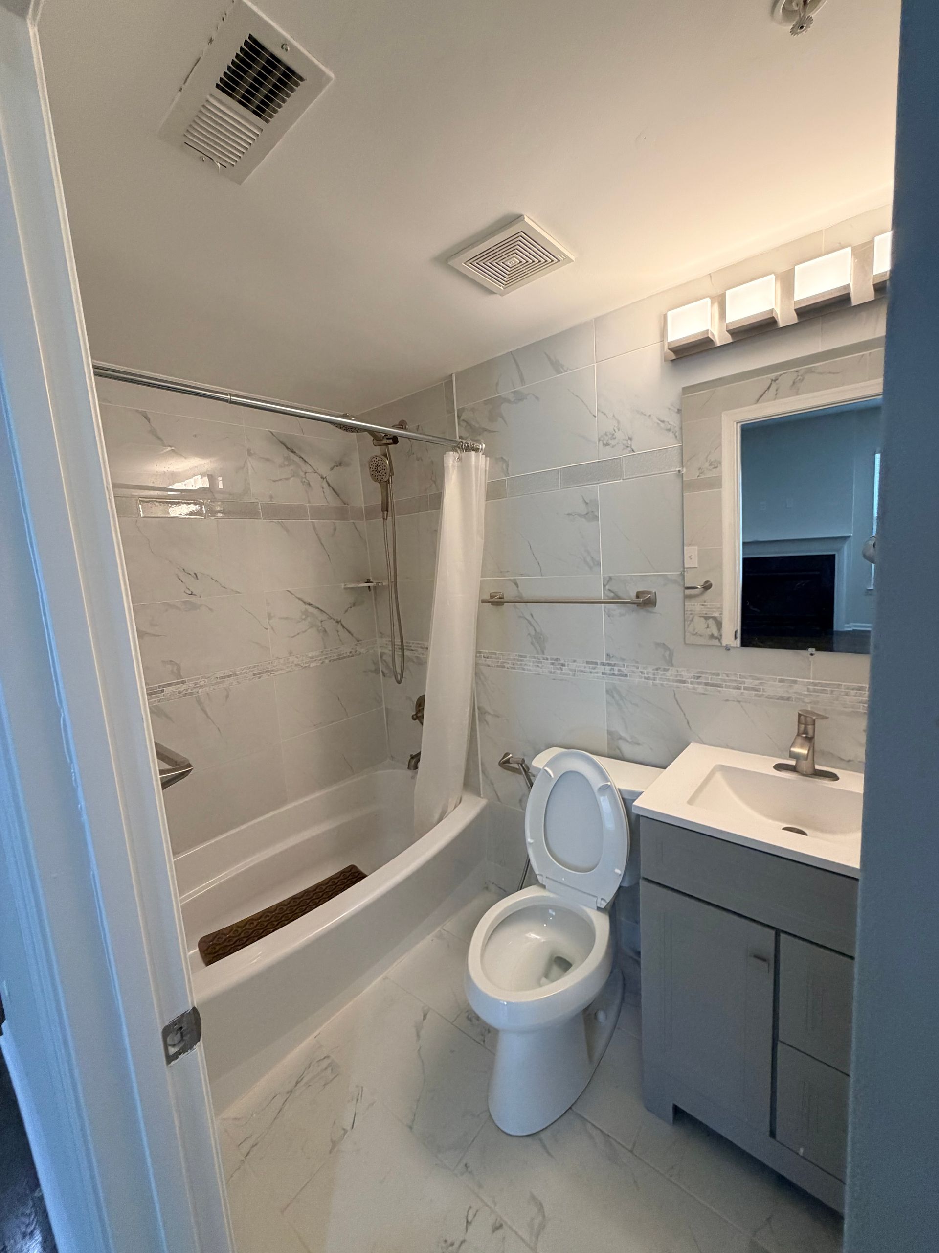 Small bathroom with bathtub, toilet, sink, gray vanity, and tiled shower walls.