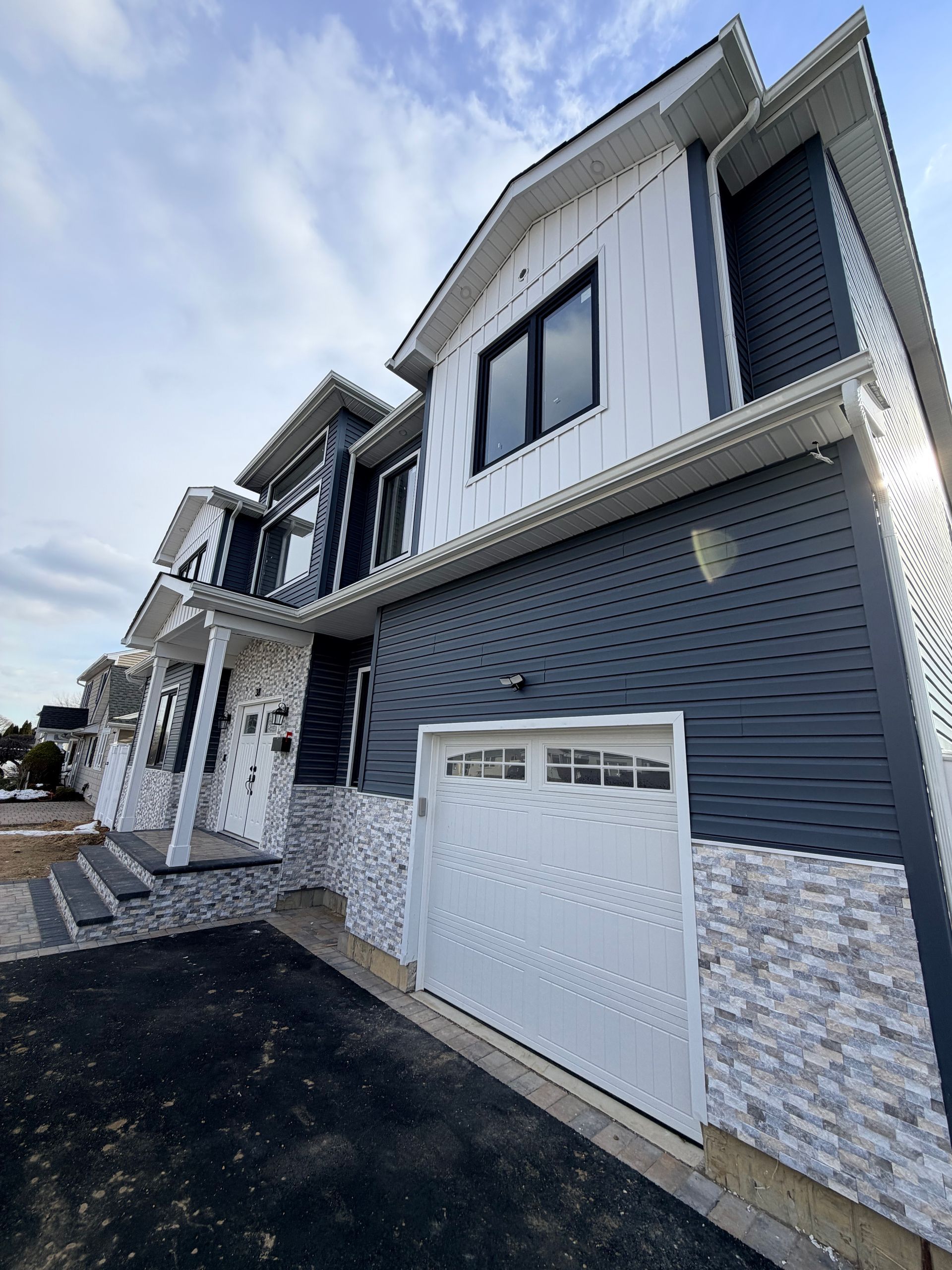 Modern two-story house exterior with white and gray siding, stone accents, garage, and driveway
