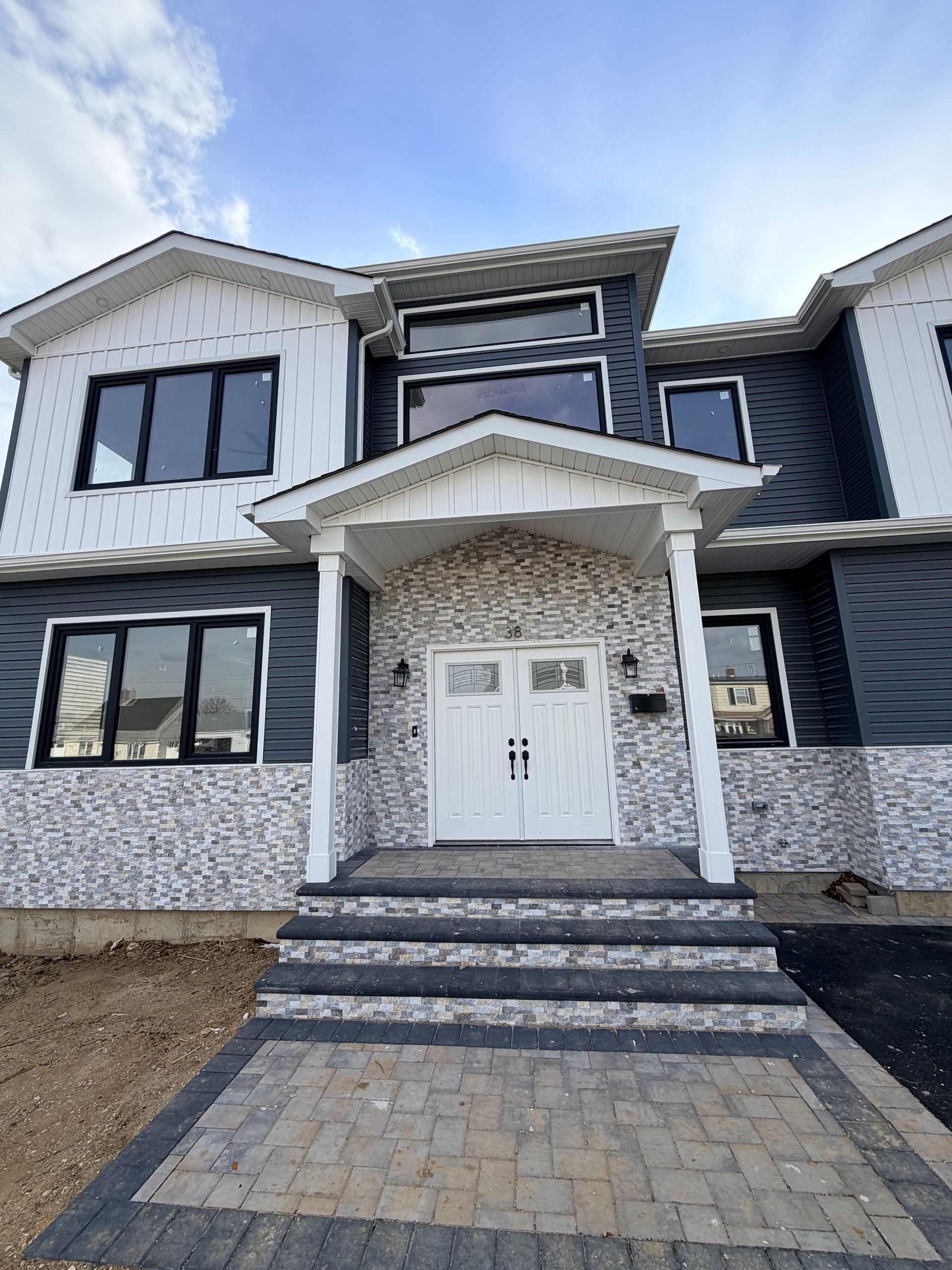 Front view of a two-story house with white and gray exterior, covered entry, and tiled walkway