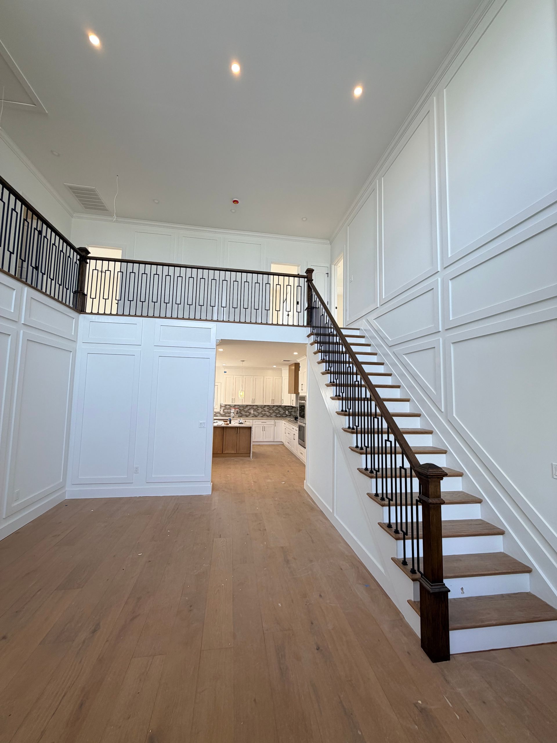 Bright hallway with white paneled walls, wood floors, and a staircase leading to an upper landing.