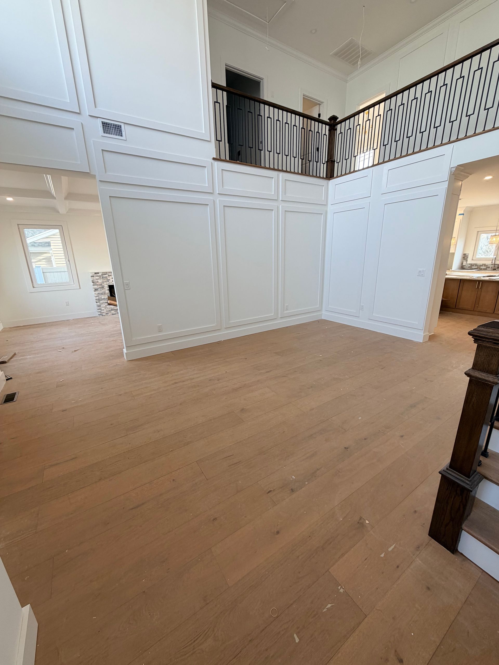 Bright open foyer with white paneled walls, wood floors, and a second-floor balcony railing