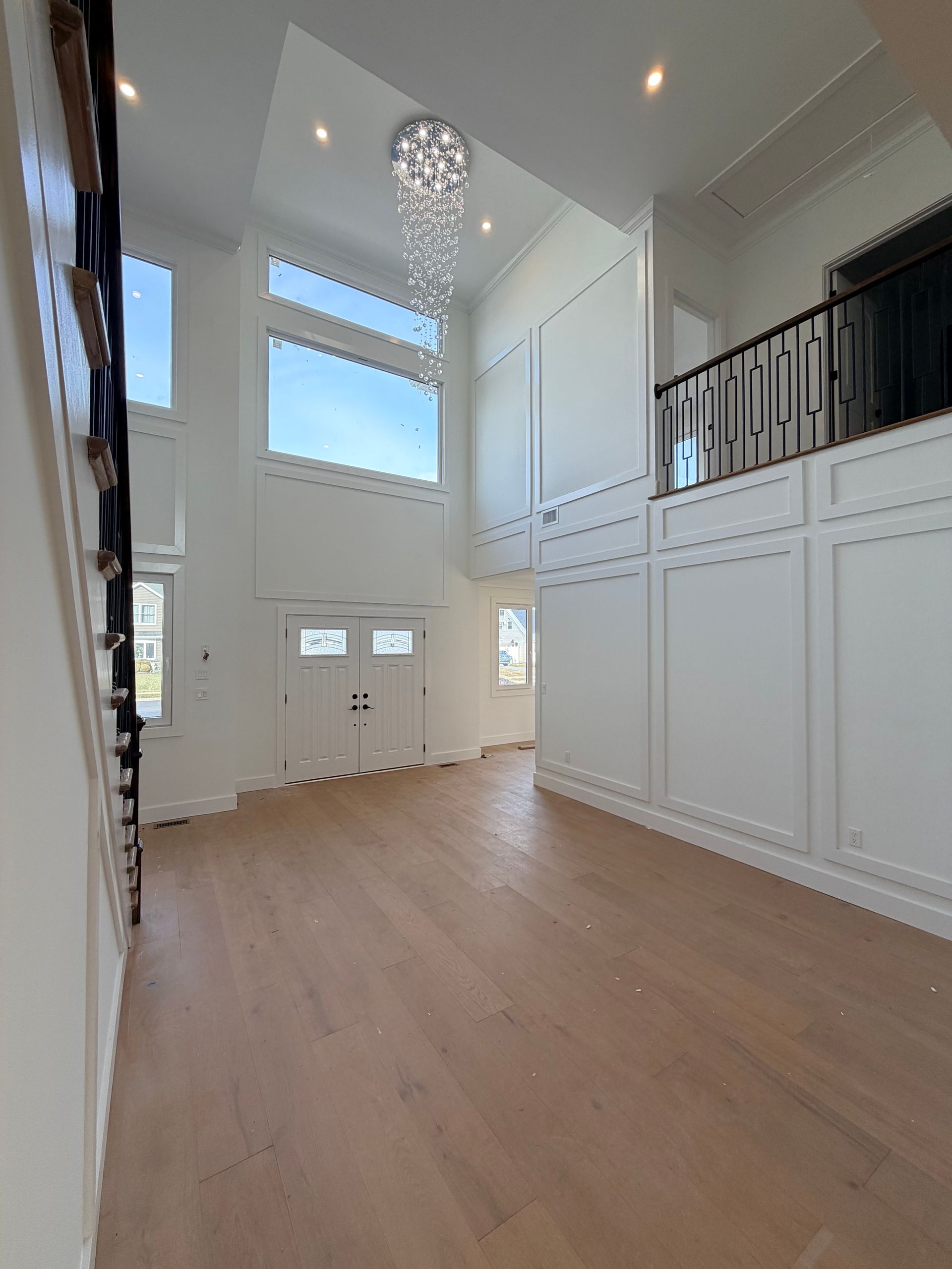 Bright, empty foyer with high ceilings, chandelier, white paneled walls, and light wood floors