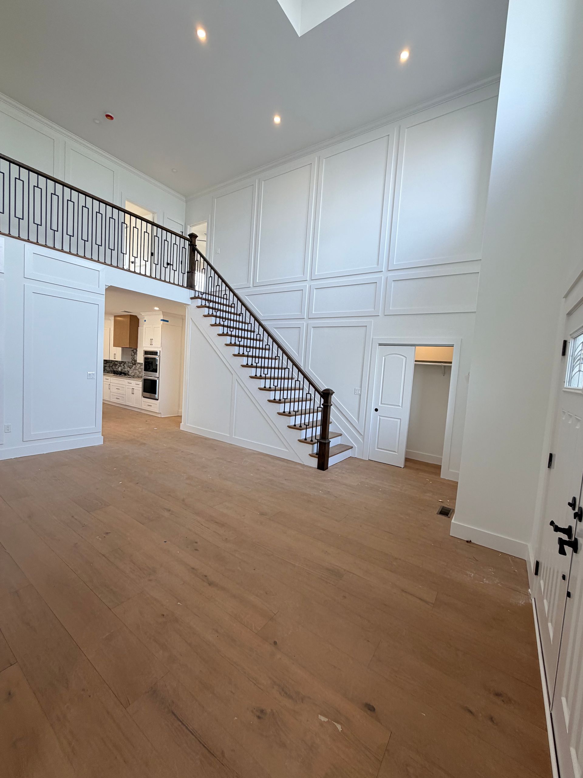 Spacious white foyer with wood floors, staircase, and high ceilings