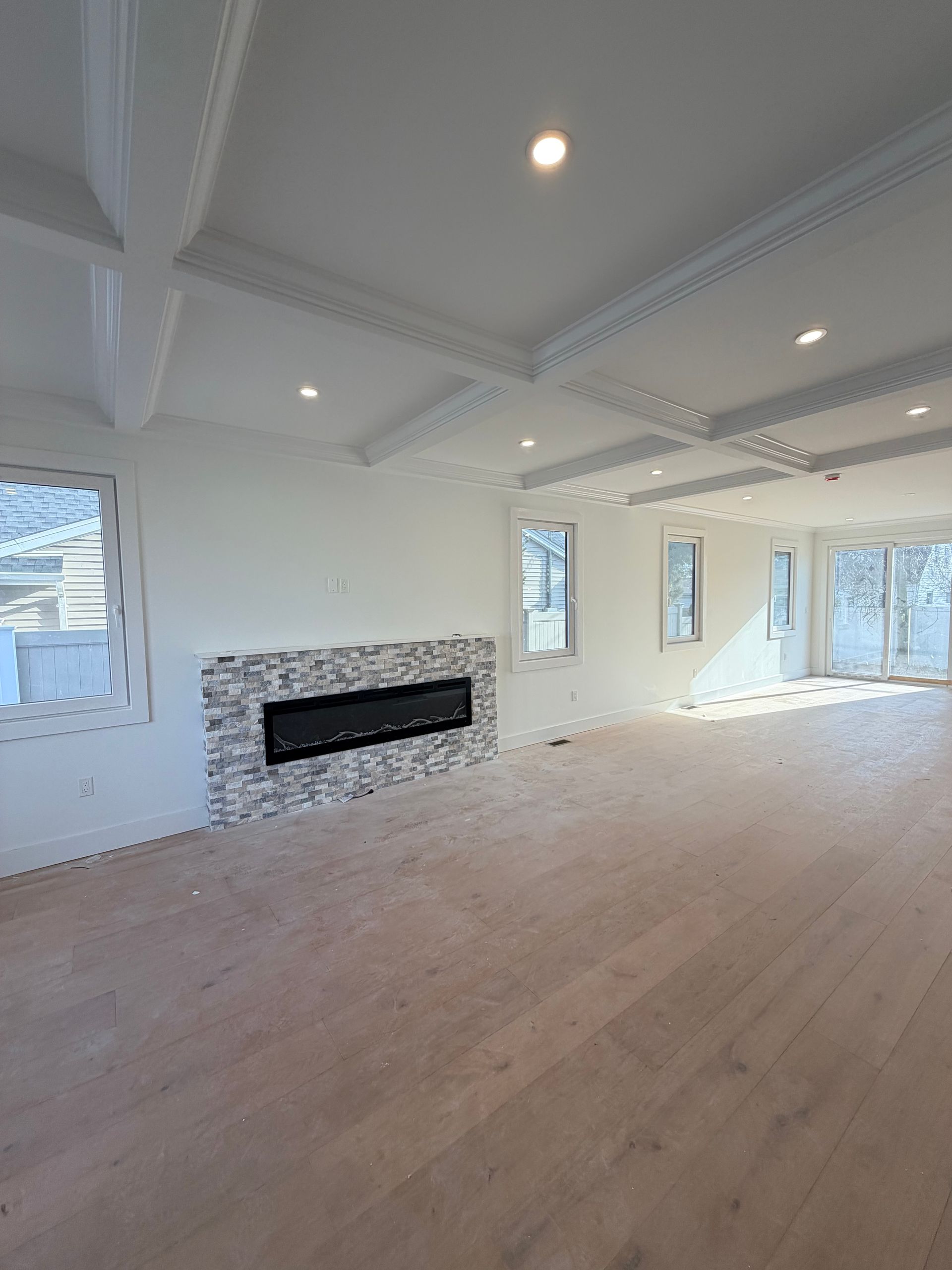 Bright empty living room with white ceilings, wood floors, recessed lights, and a modern fireplace.