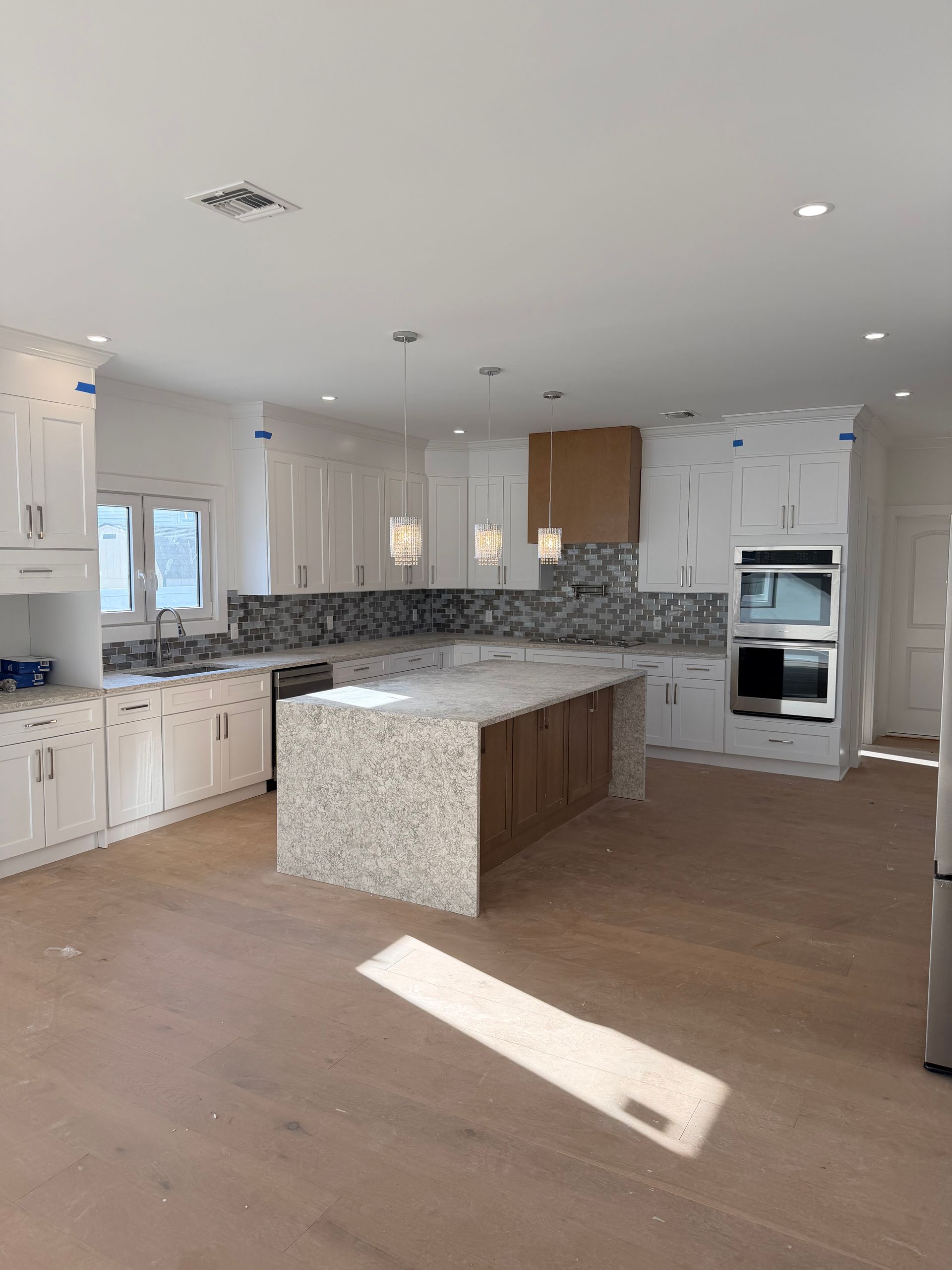 Bright modern kitchen with white cabinets, marble island, gray backsplash, and wood floors.