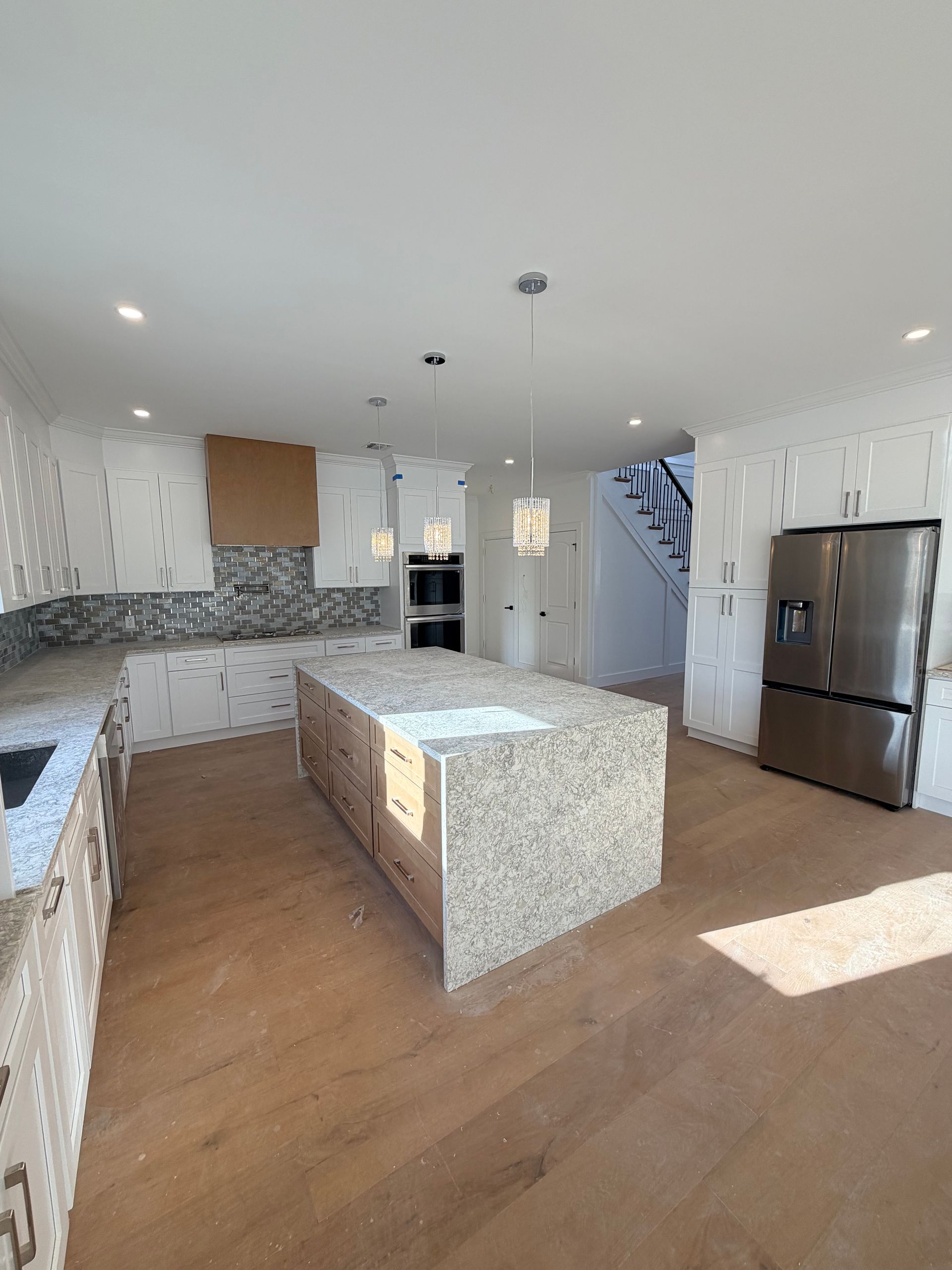 Bright modern kitchen with granite island, stainless steel fridge, white cabinets, and wood floors.