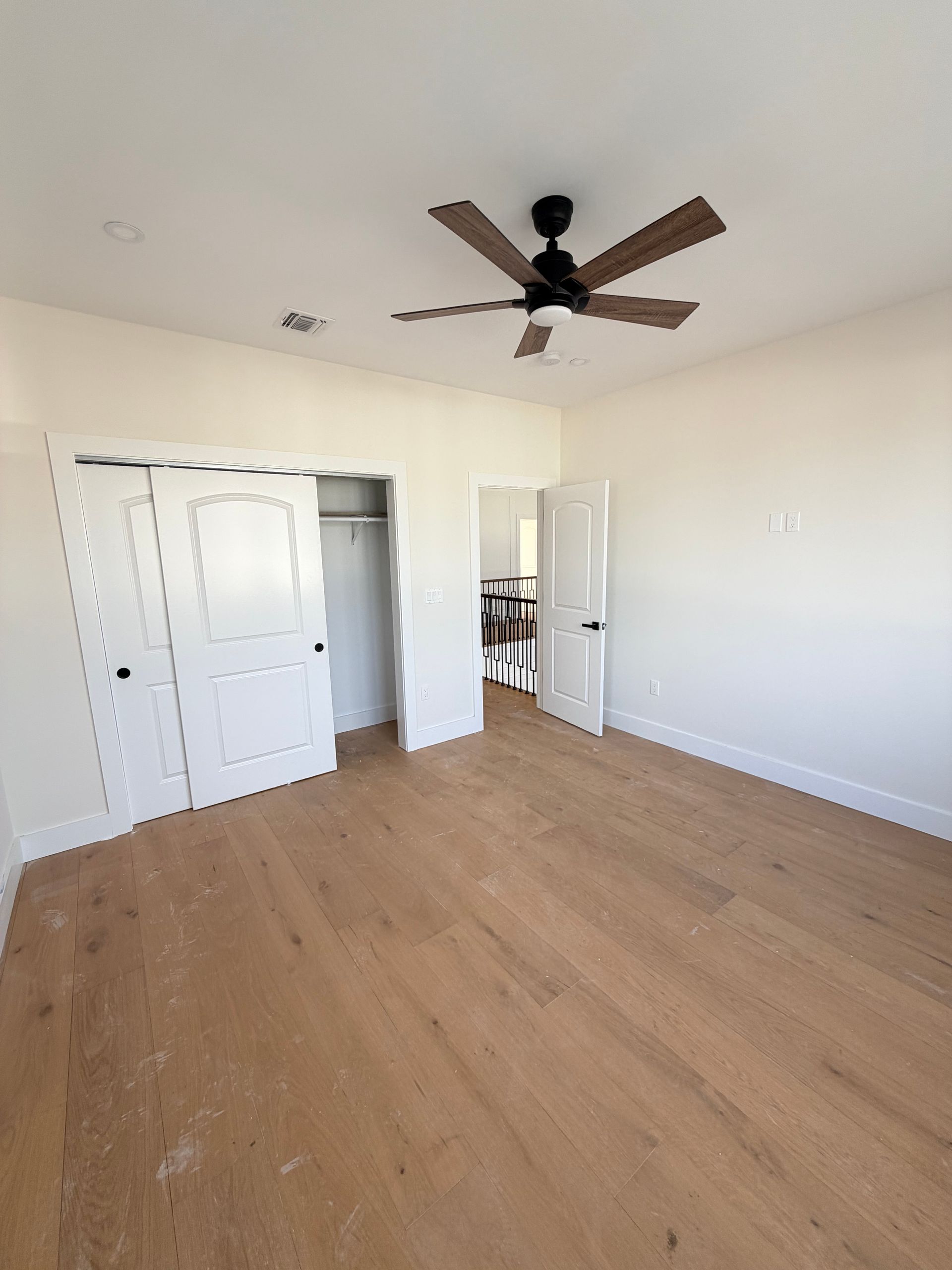 Empty white bedroom with wood floors, ceiling fan, and double closet doors