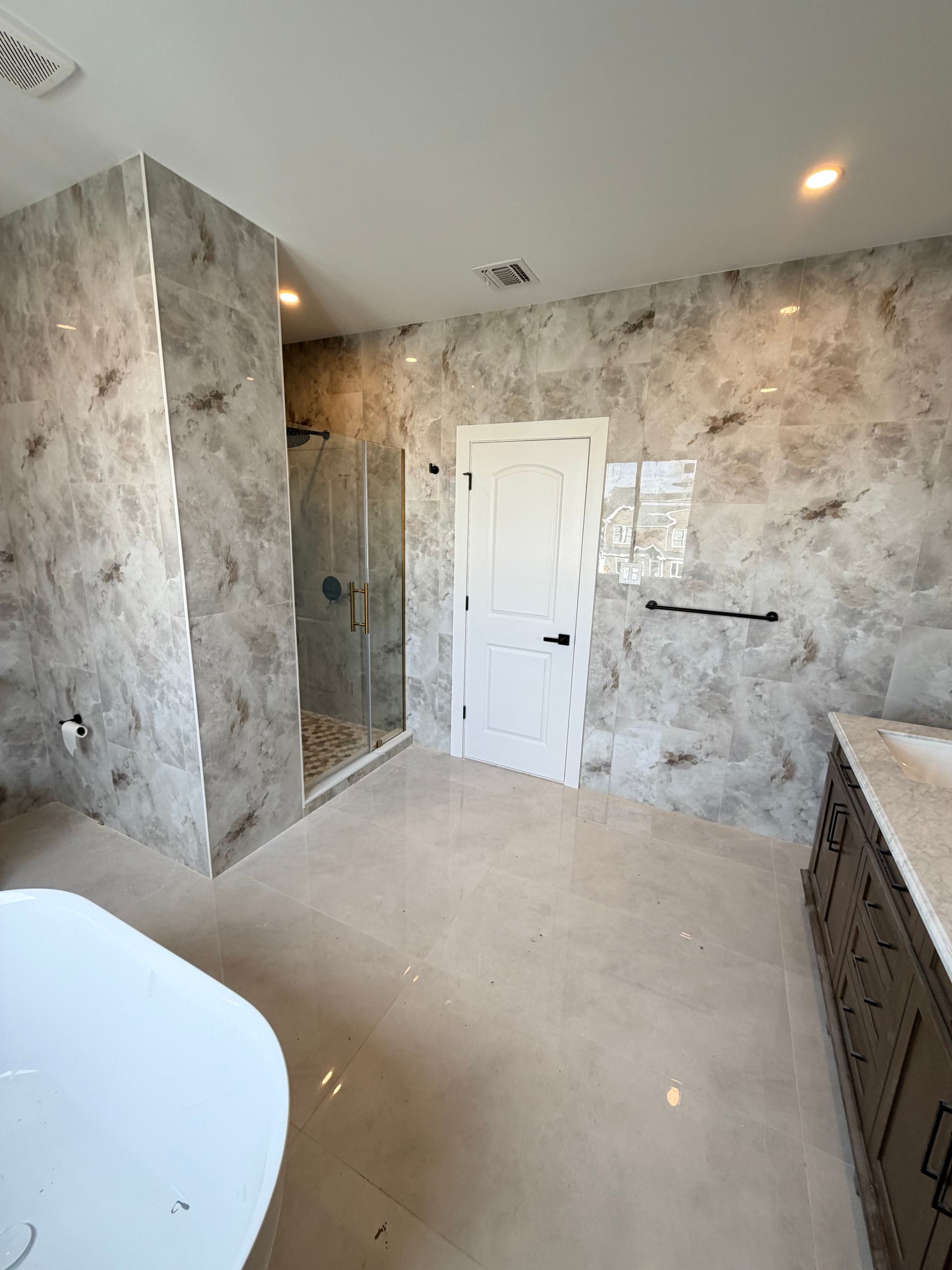 Modern bathroom with gray marble-pattern walls, white door, walk-in shower, and dark vanity.