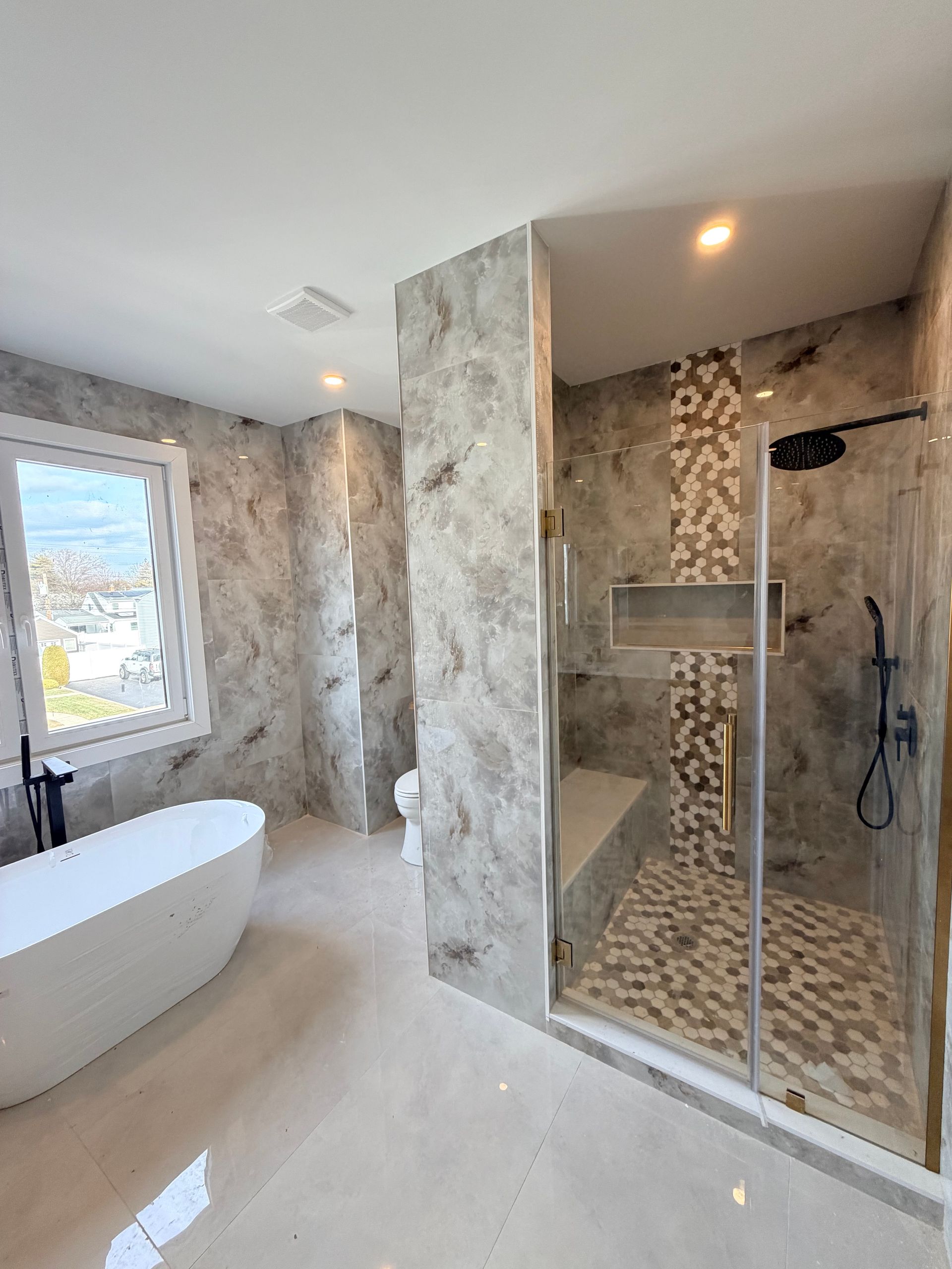 Modern bathroom with freestanding tub, walk-in glass shower, and marble-look walls and floor