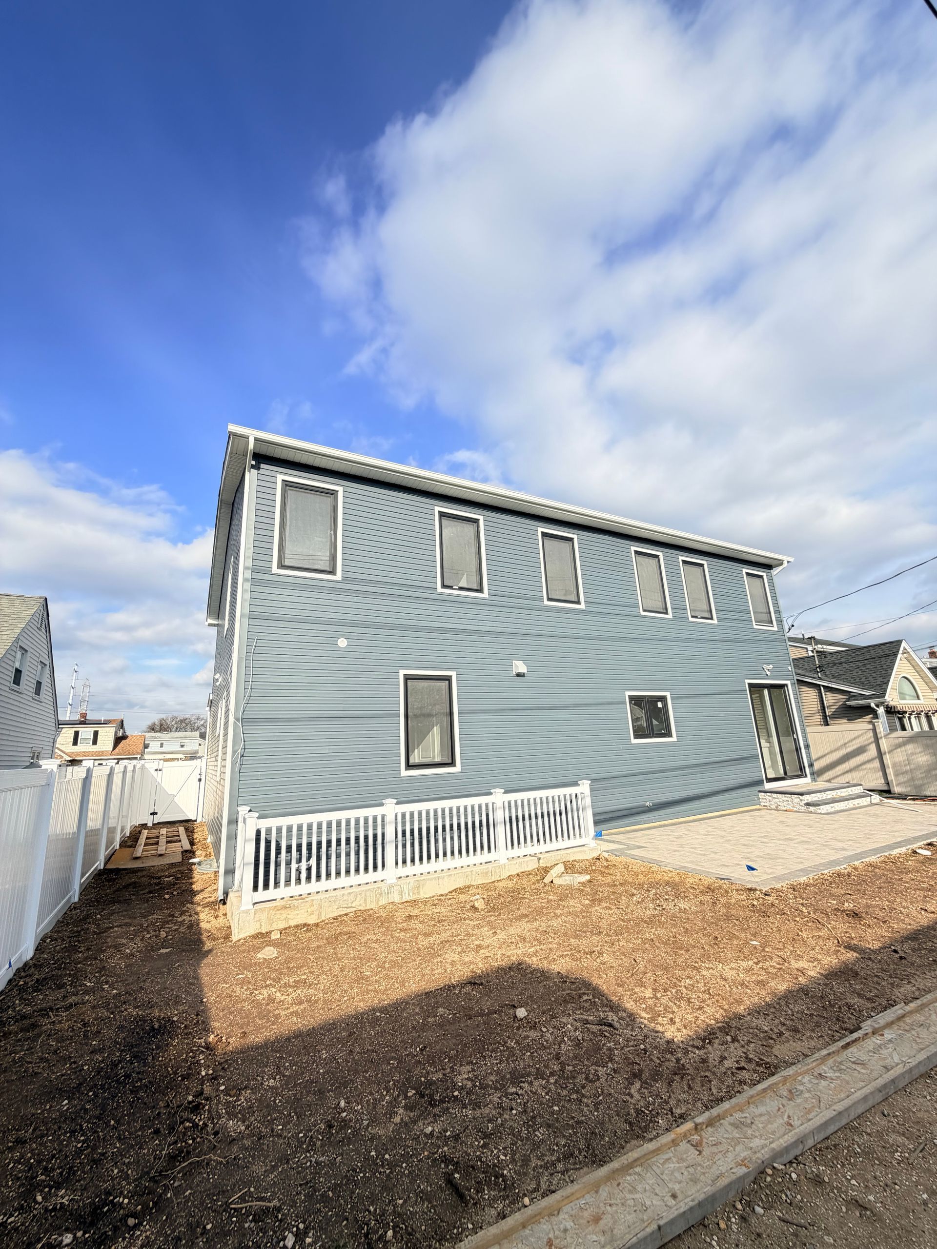 Gray house with white trim and small porch, seen from the side under a blue sky with clouds.