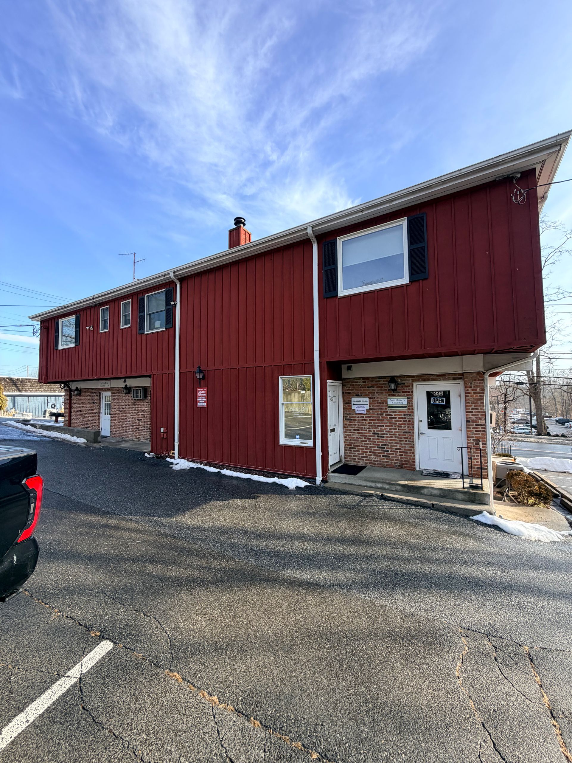 Red townhouse-style building with white trim and stone base beside a parking lot under a blue sky