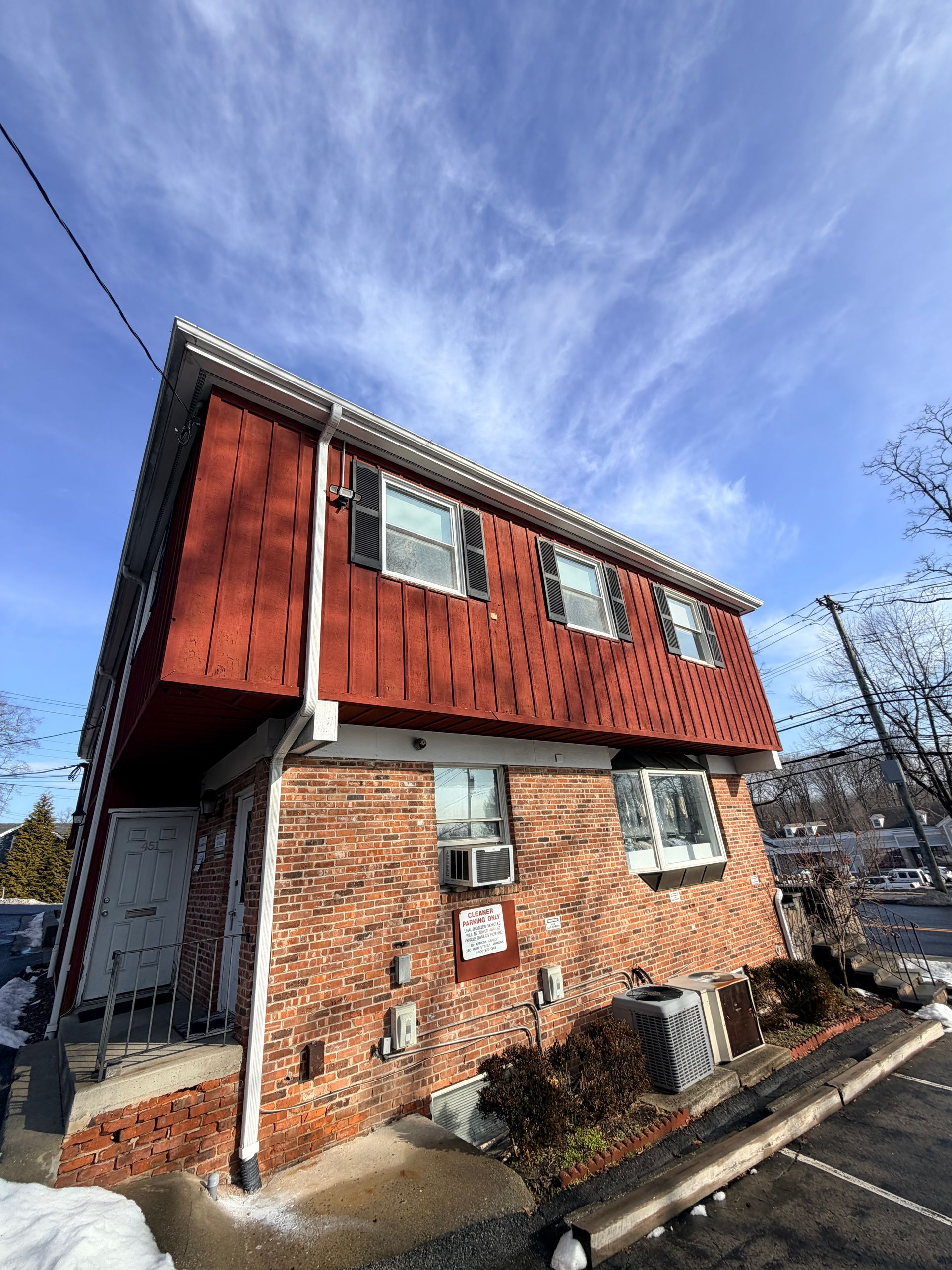 Two-story brick and red-clad house with white-framed windows under a blue sky.