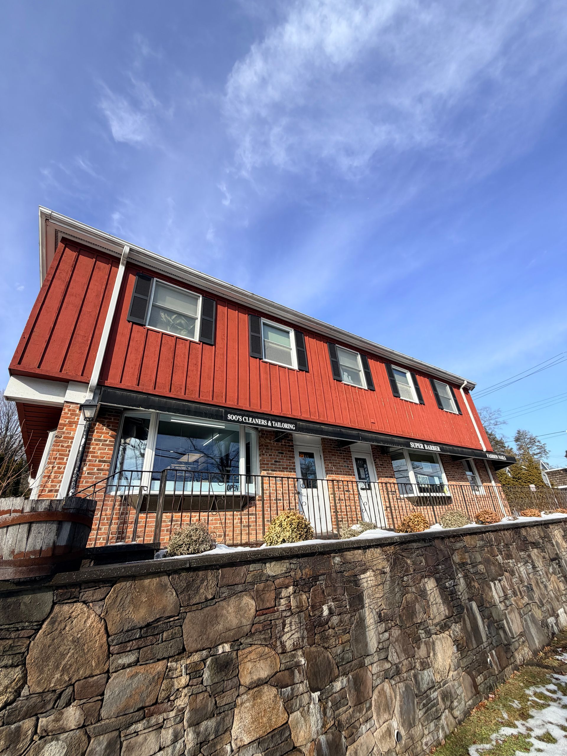 Red-roofed stone house with dormer windows behind a stone wall under a blue sky