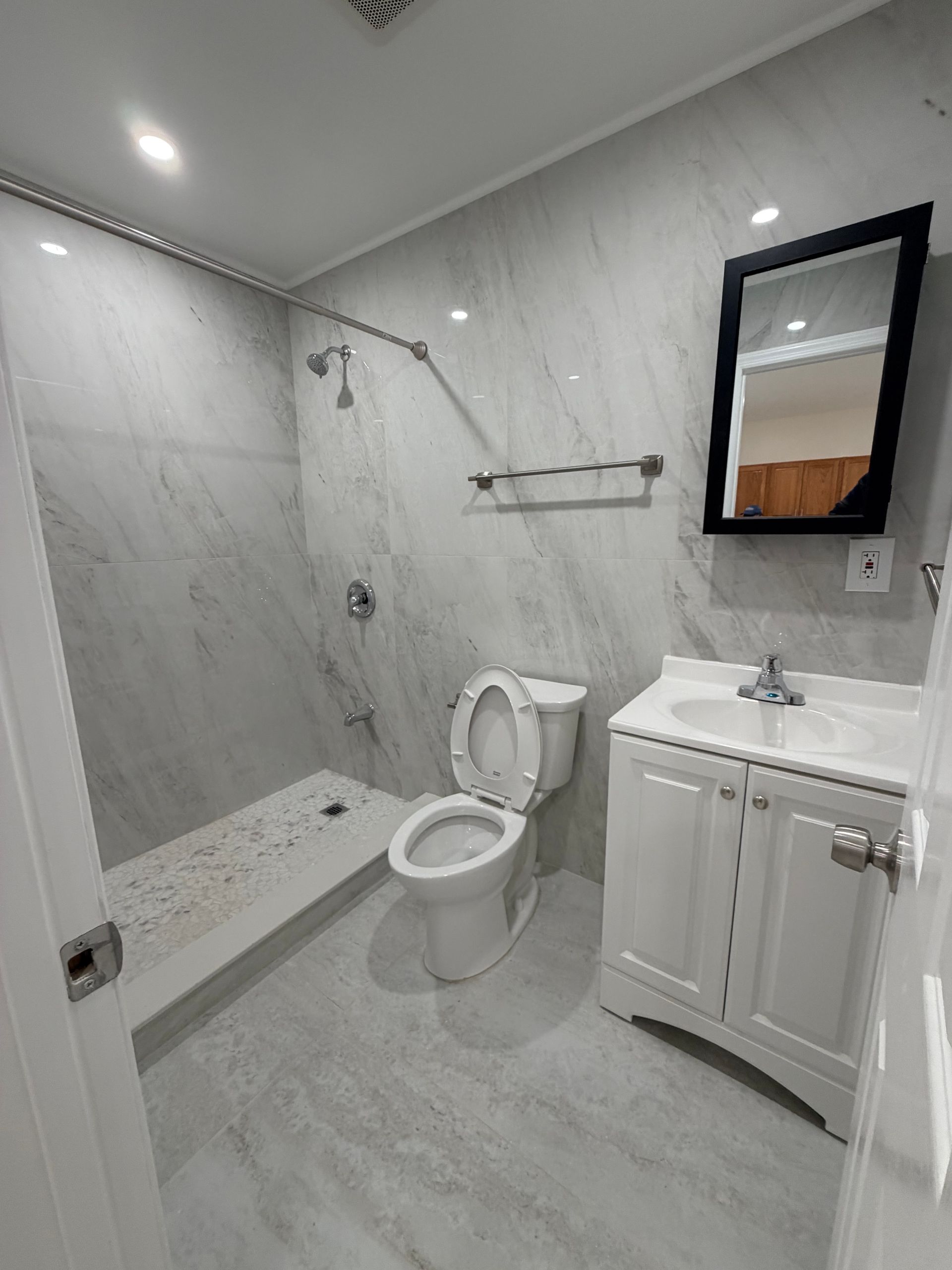 Modern white bathroom with walk-in shower, toilet, sink vanity, and wall mirror.