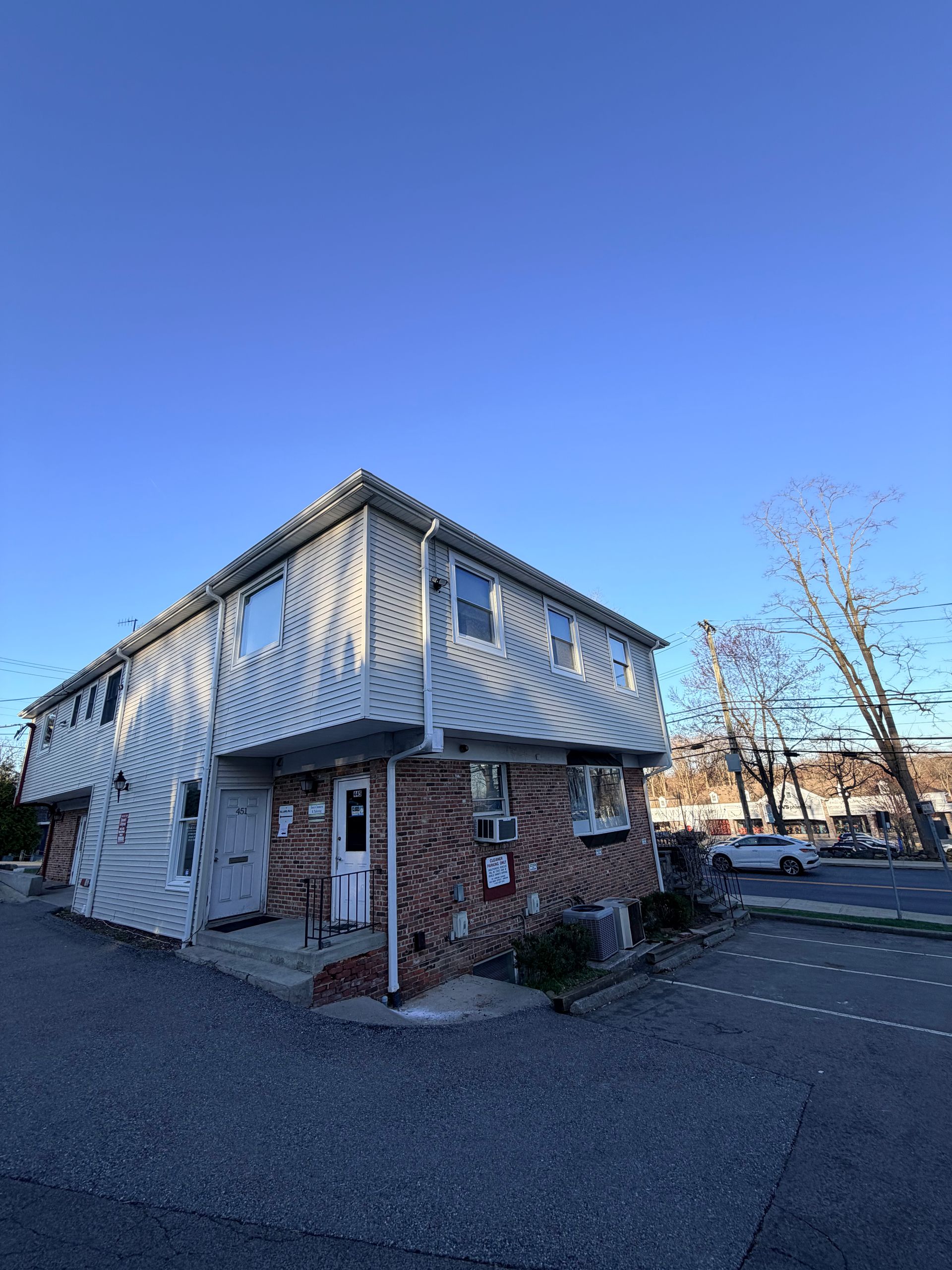 Small brick building with white trim and awnings beside an empty parking lot under a blue sky