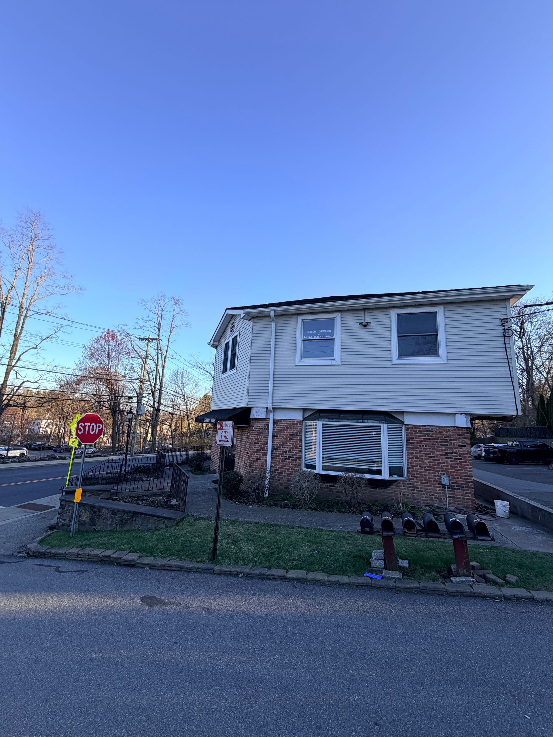 Two-story white and brick house at a street corner with a stop sign under a clear blue sky