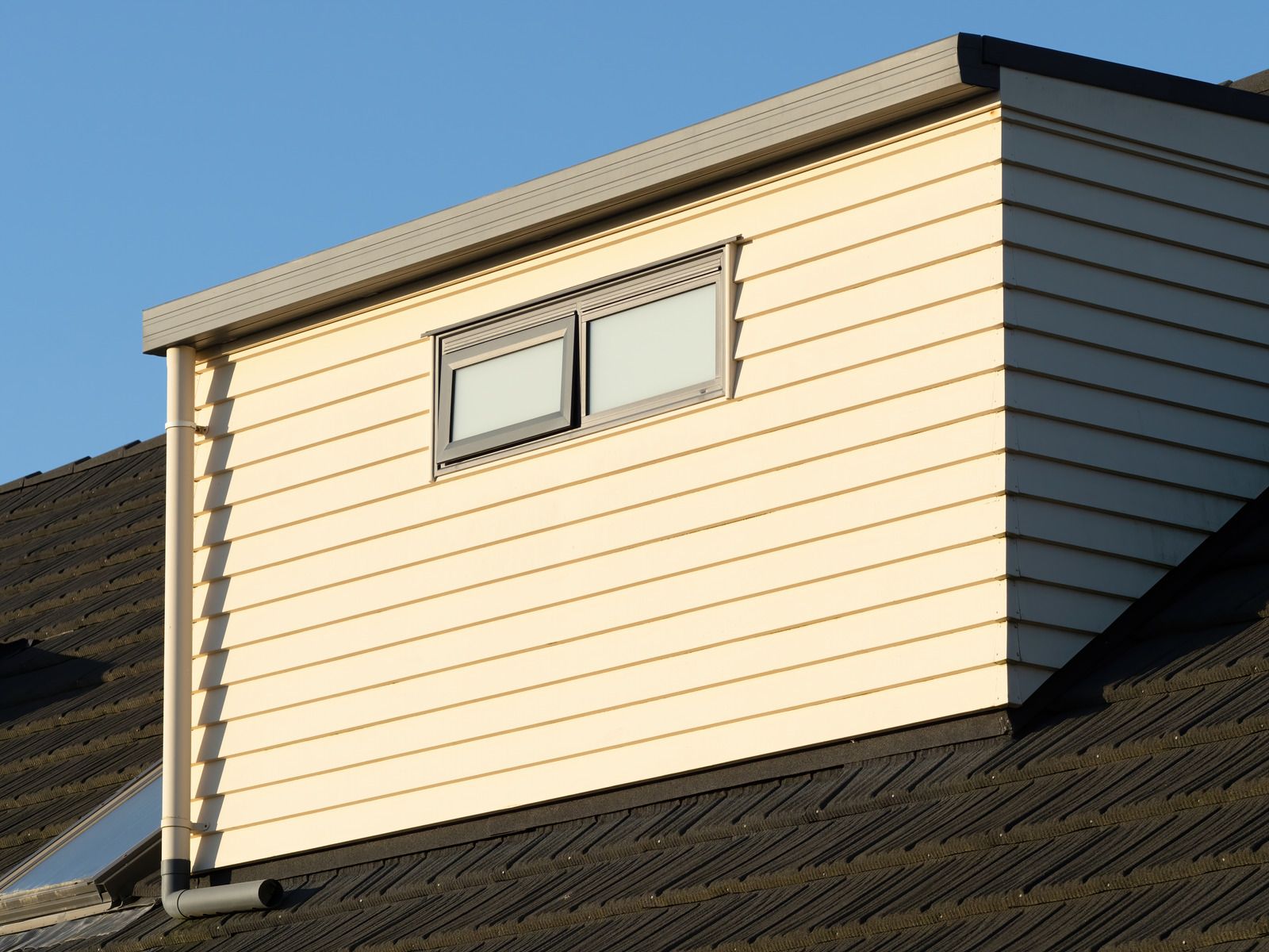 Dormer window on a beige house roof under blue sky