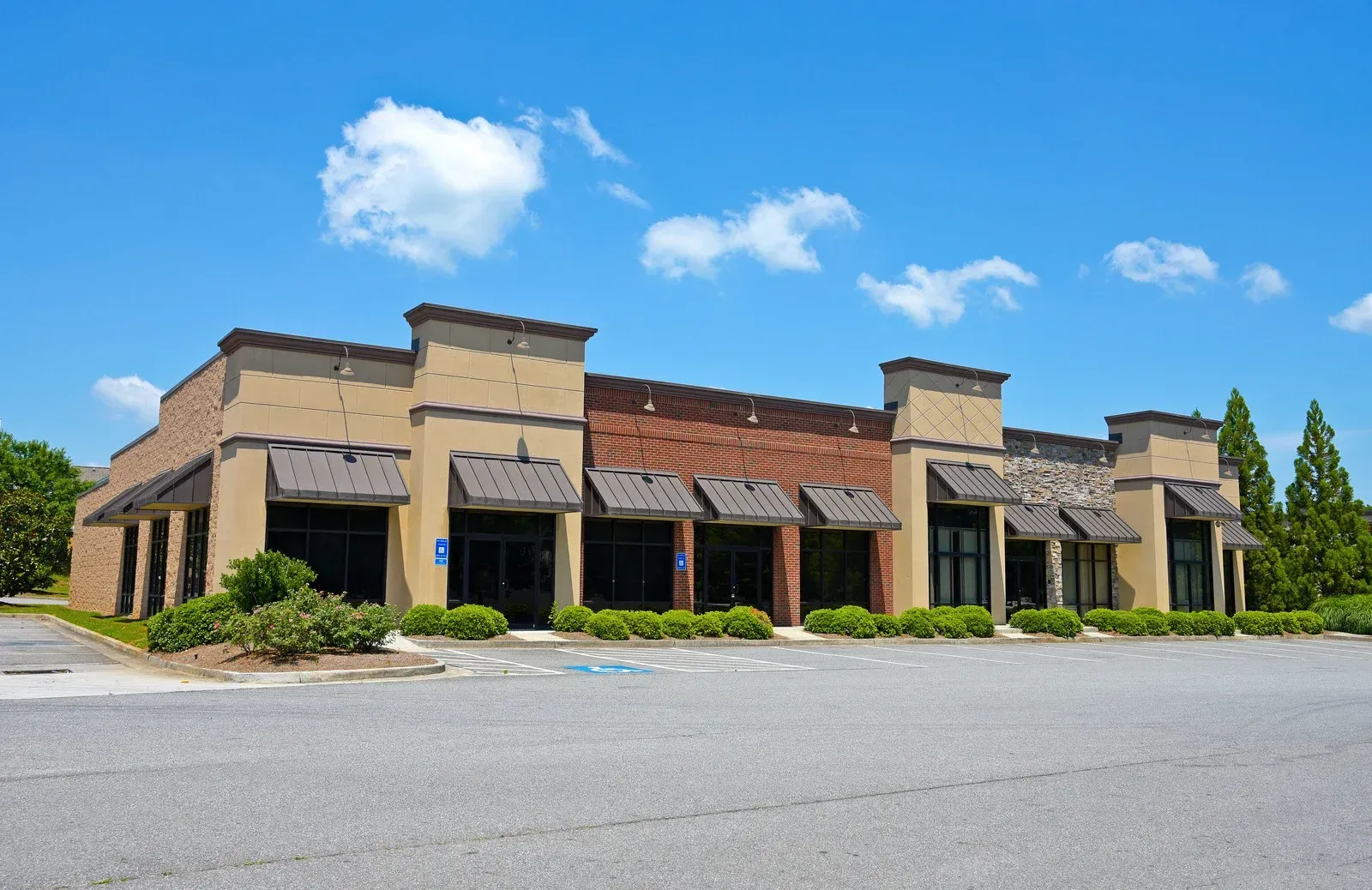 Single-story tan commercial building with red awnings under a blue sky, viewed from an empty parking lot