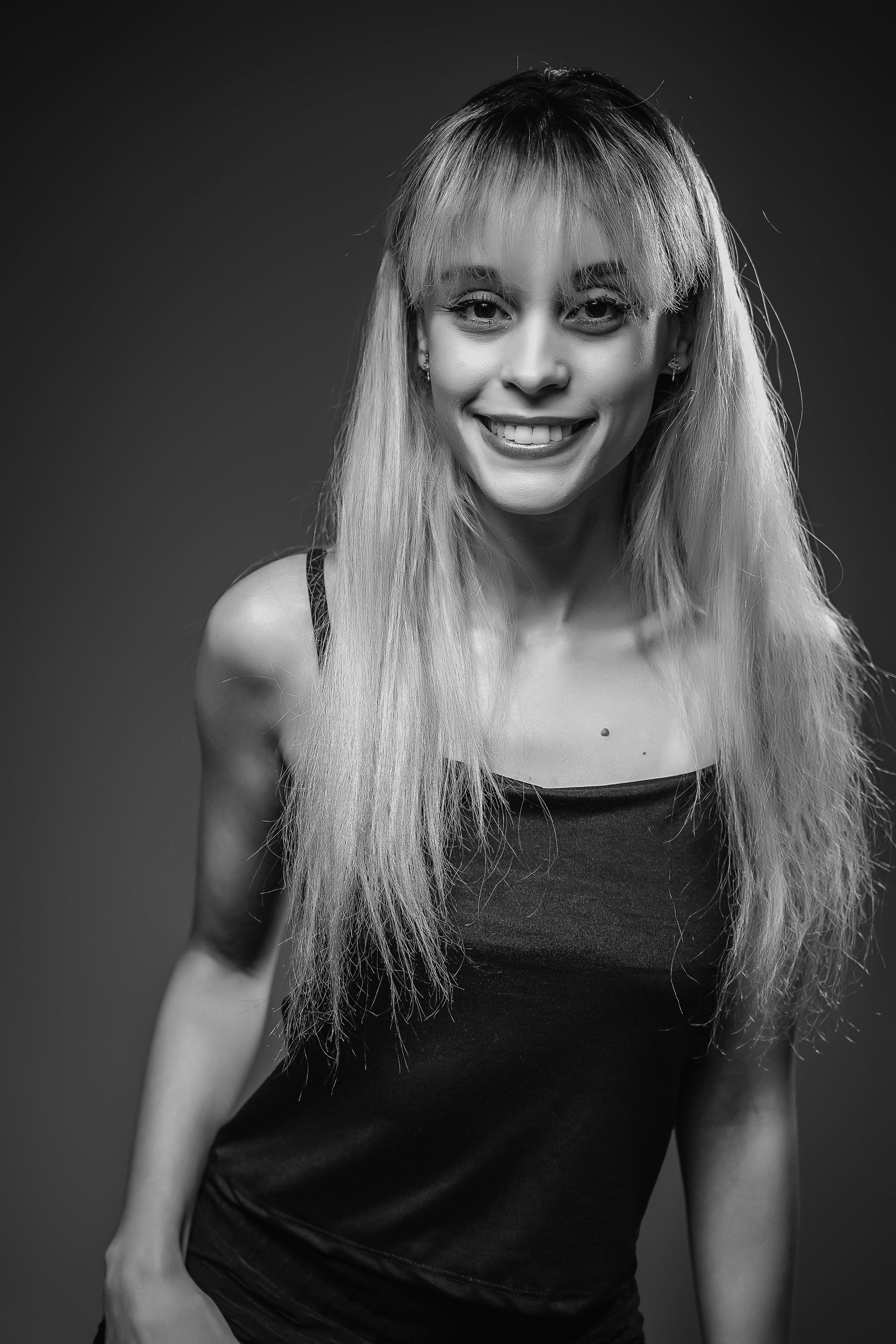 Retrato de estúdio em preto e branco de uma pessoa sorridente com longos cabelos ondulados, vestindo uma blusa escura.