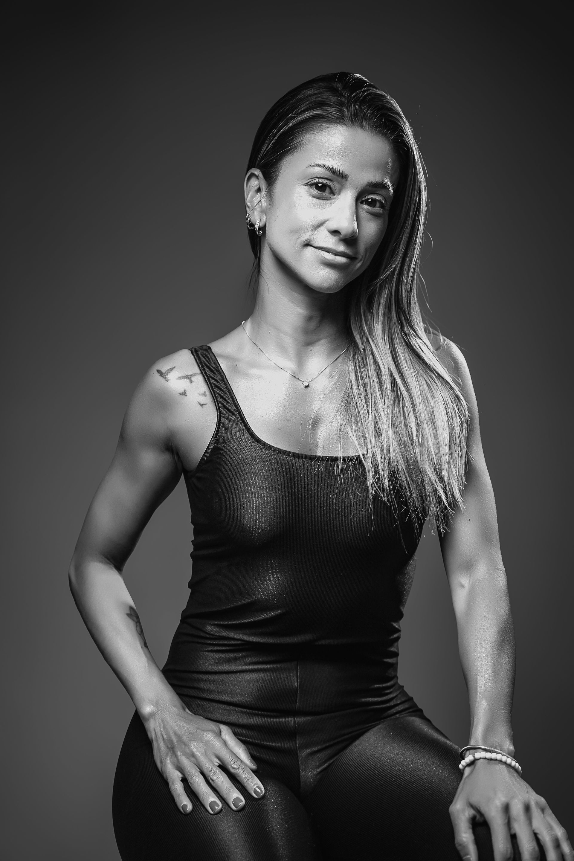 Retrato de uma pessoa com cabelo crespo, posando com uma regata escura contra um fundo liso.