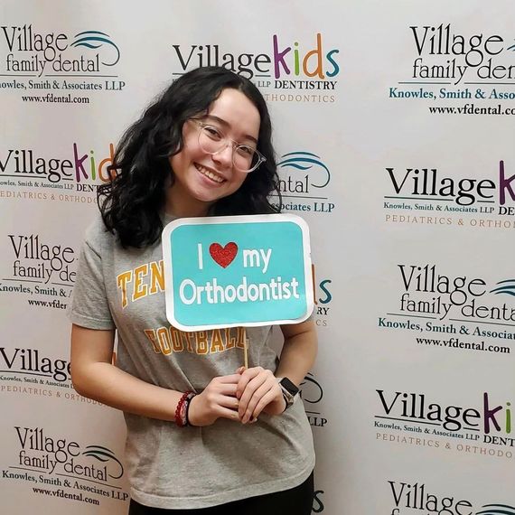 A woman is holding a sign that says `` i love my orthodontist ''.
