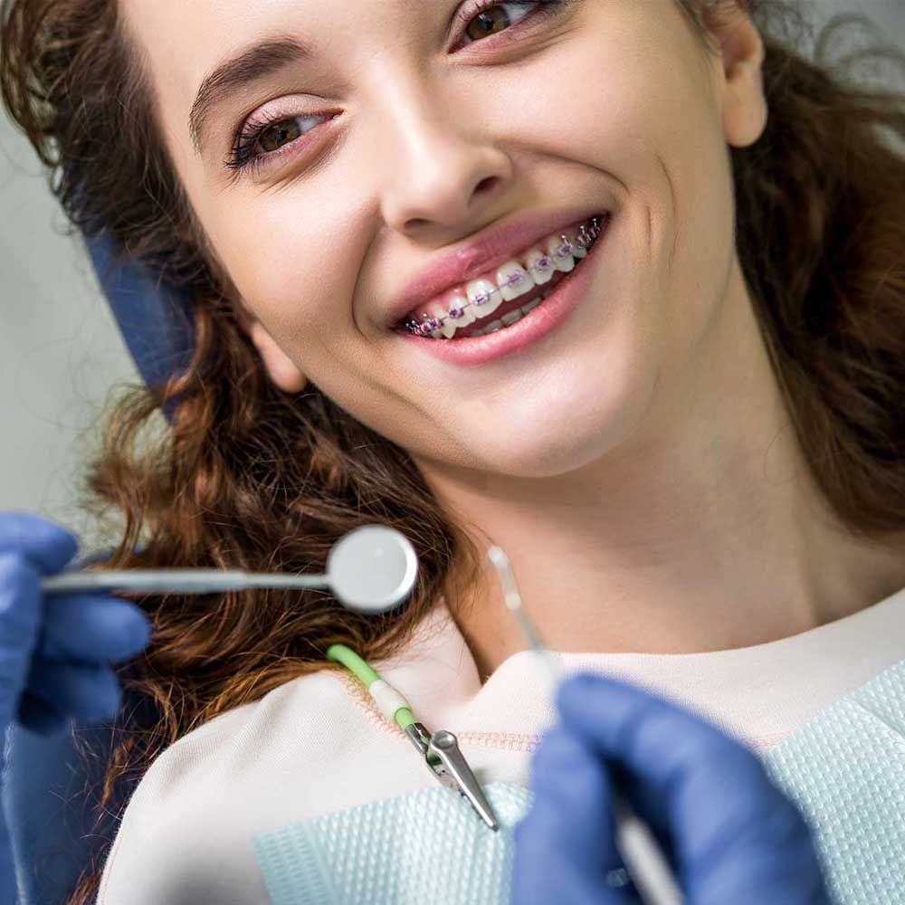 close up of cheerful woman in braces during examination of teeth near dentist