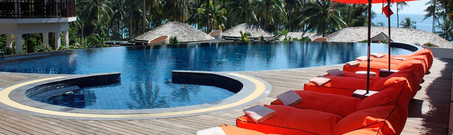 Piscina do resort com espreguiçadeiras vermelhas, água azul e pátio sombreado por palmeiras.