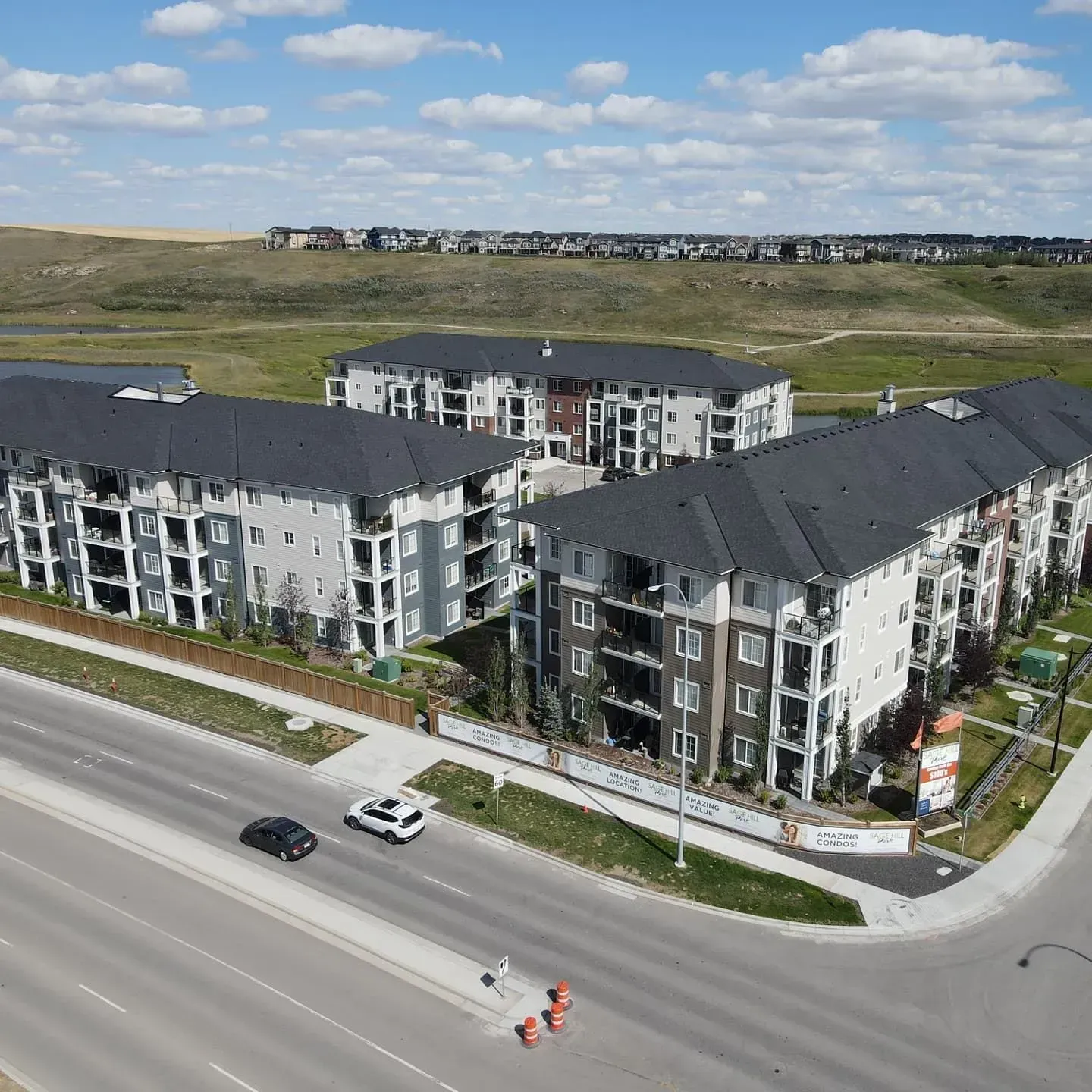 Aerial view of a modern apartment complex beside a wide road under a partly cloudy sky.