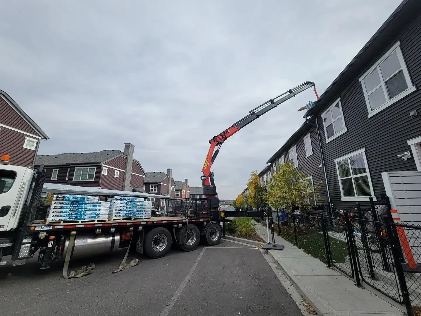 Crane truck lifting materials beside a dark-brick house on a residential street