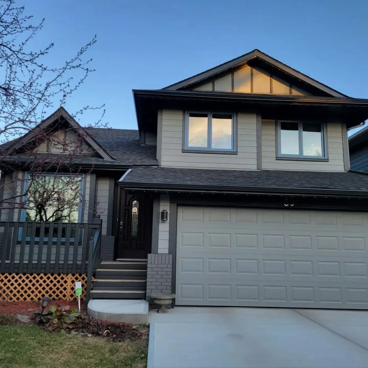 Two-story beige house with a gray garage, front steps, and a small porch at dusk