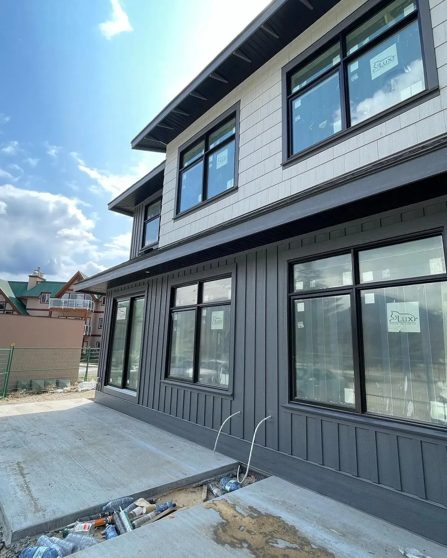 Two-story house exterior with dark siding, large windows, and a concrete walkway under construction