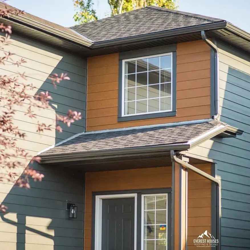 Two-story house exterior with gray siding, tan trim, and a covered front entry
